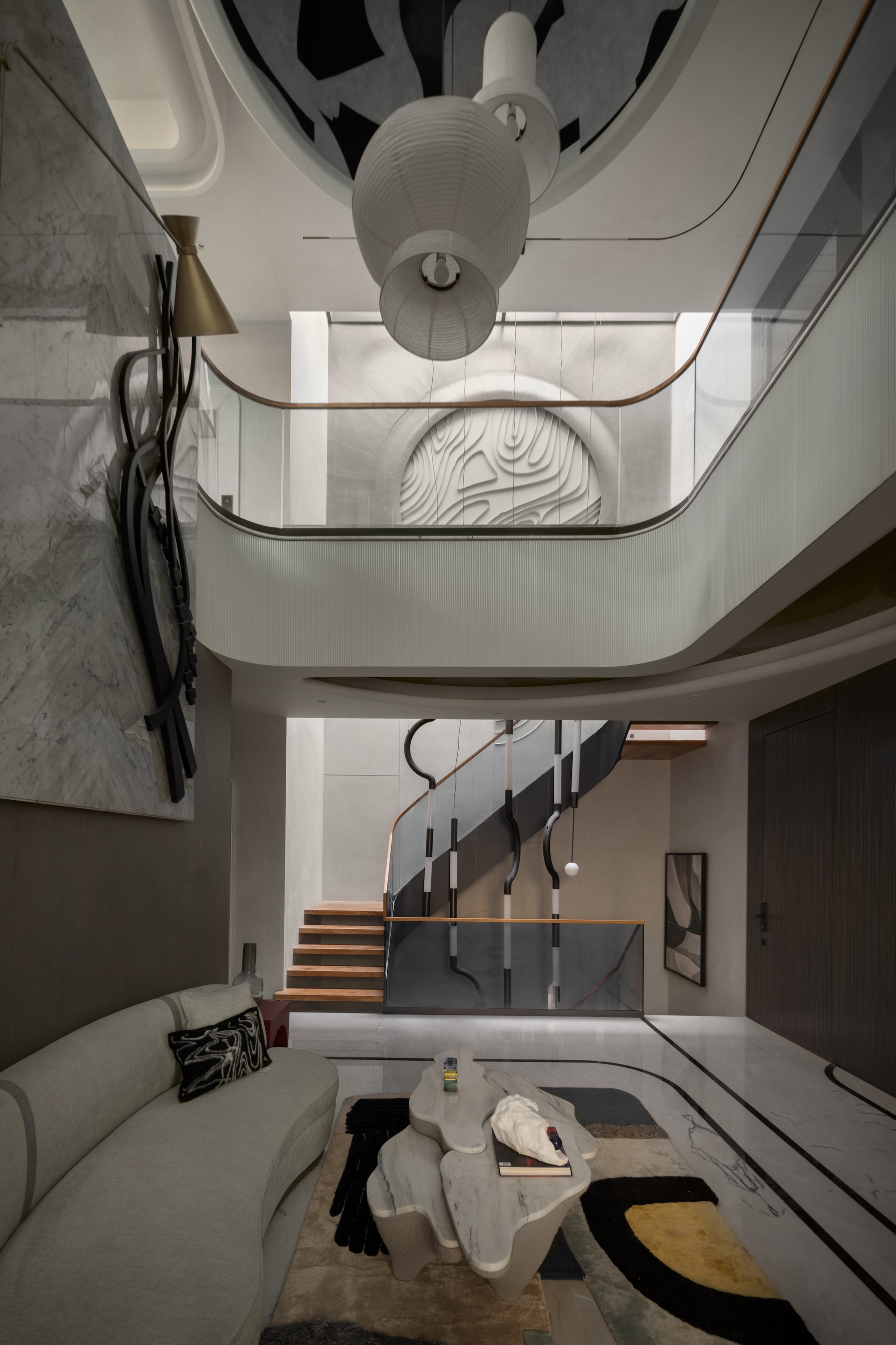 Double-height living space with a curved mezzanine balustrade, paper pendant lamps and a carved circular relief on the far wall
