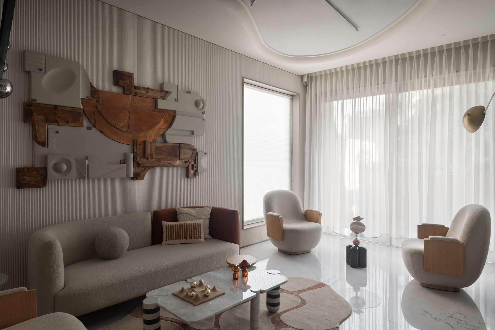 Living room with a curved sofa, sculptural timber wall relief and swivel armchairs beside sheer curtains filled with daylight