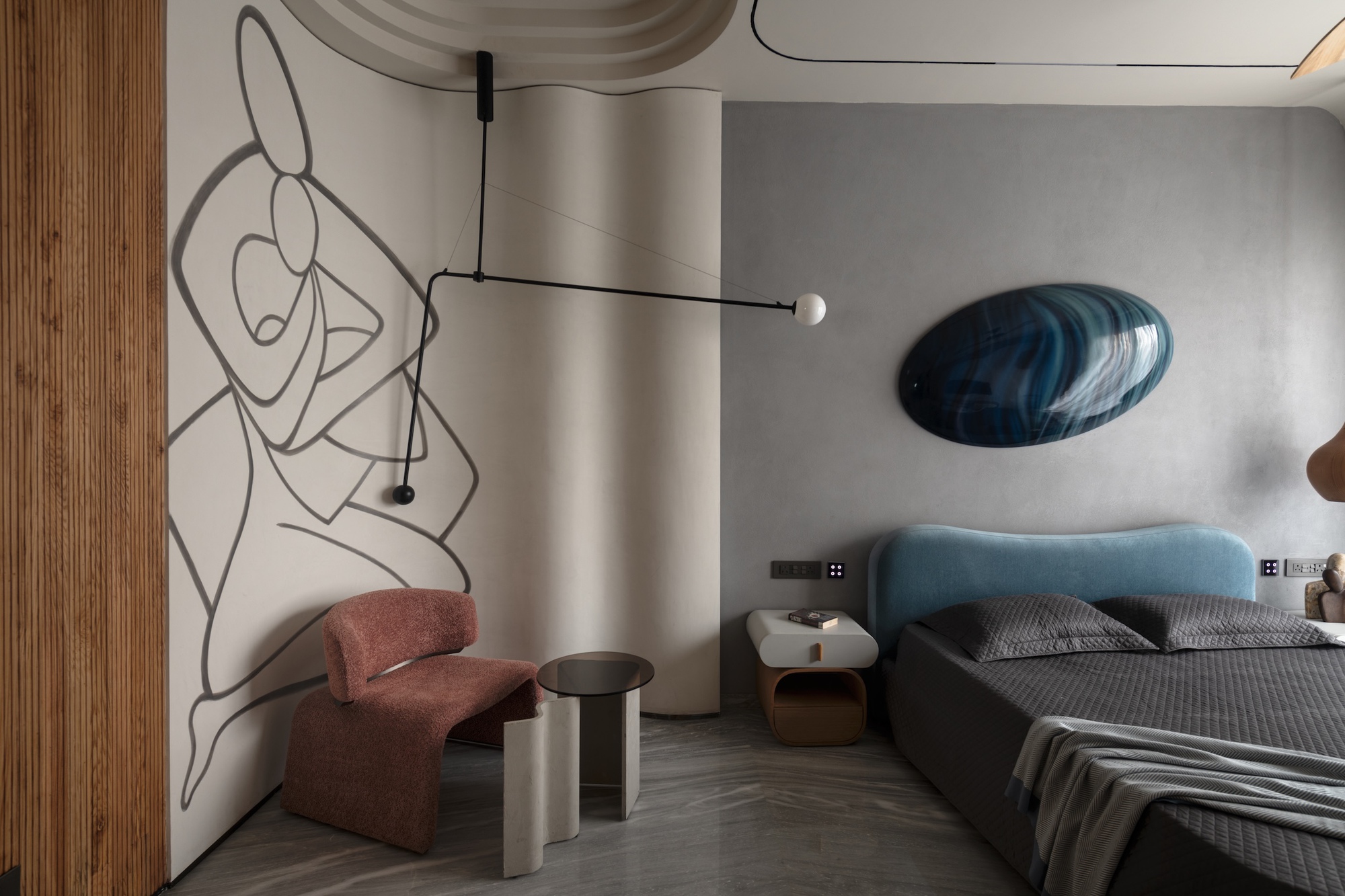 Bedroom corner with a line-drawn figure mural, a rust-pink armchair, a pivoting pendant lamp and a blue headboard
