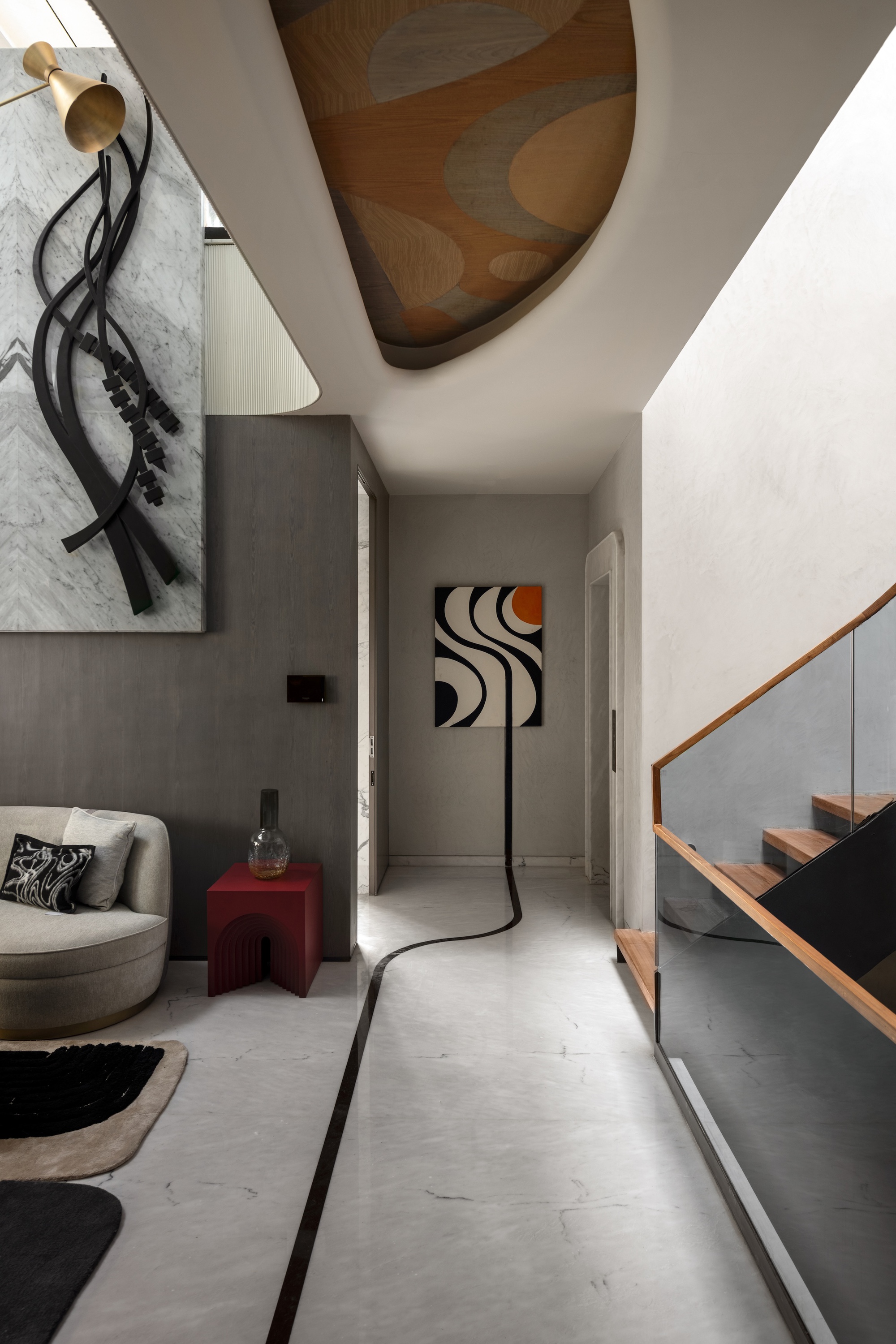 Entry passage with a black inlay line running across the marble floor, a sculptural wall relief and a glass-railed timber stair