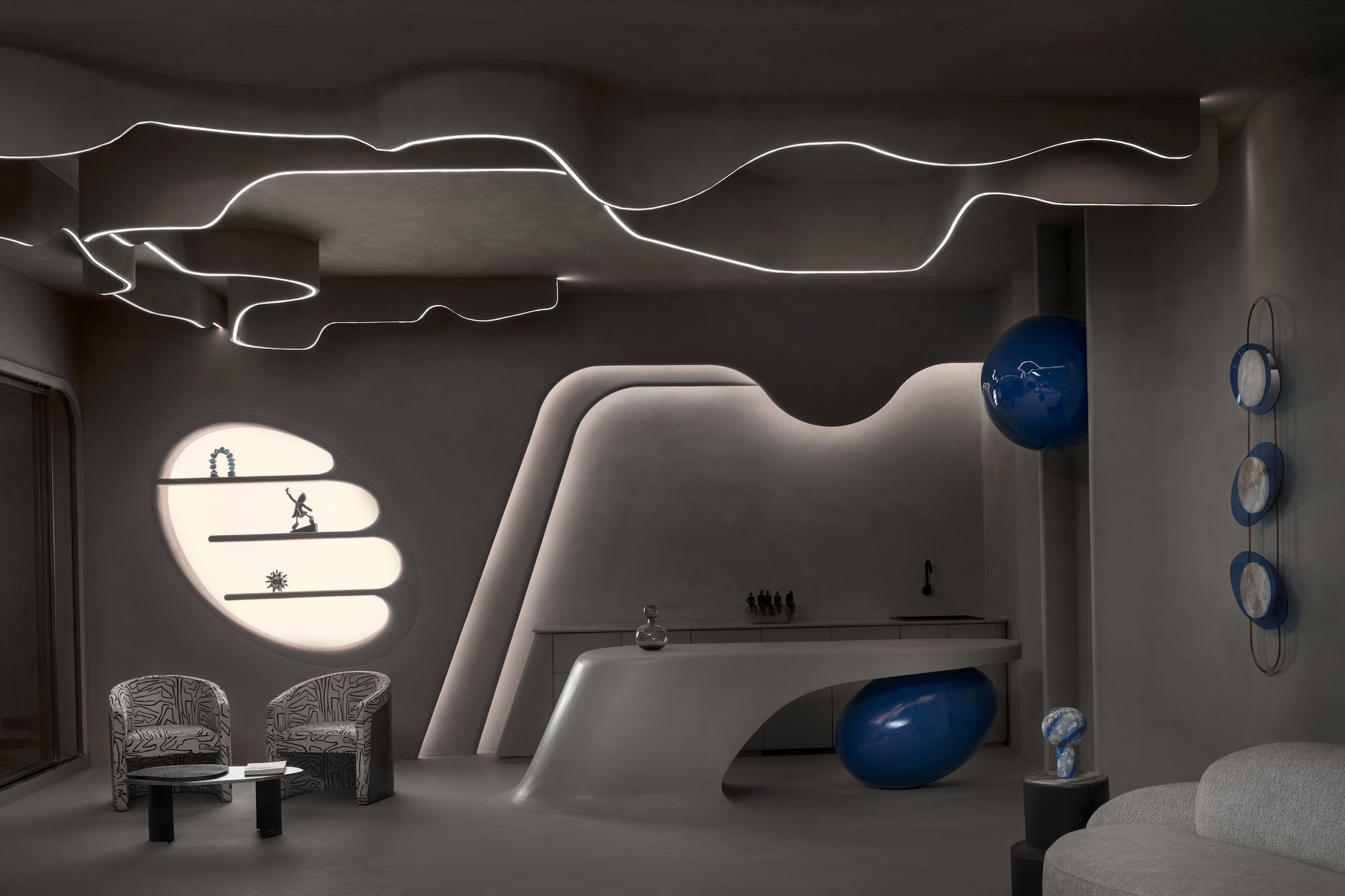 Dim lounge with a sculpted pale counter, glowing ribbon ceiling lights, a blue sphere and a backlit oval shelf niche