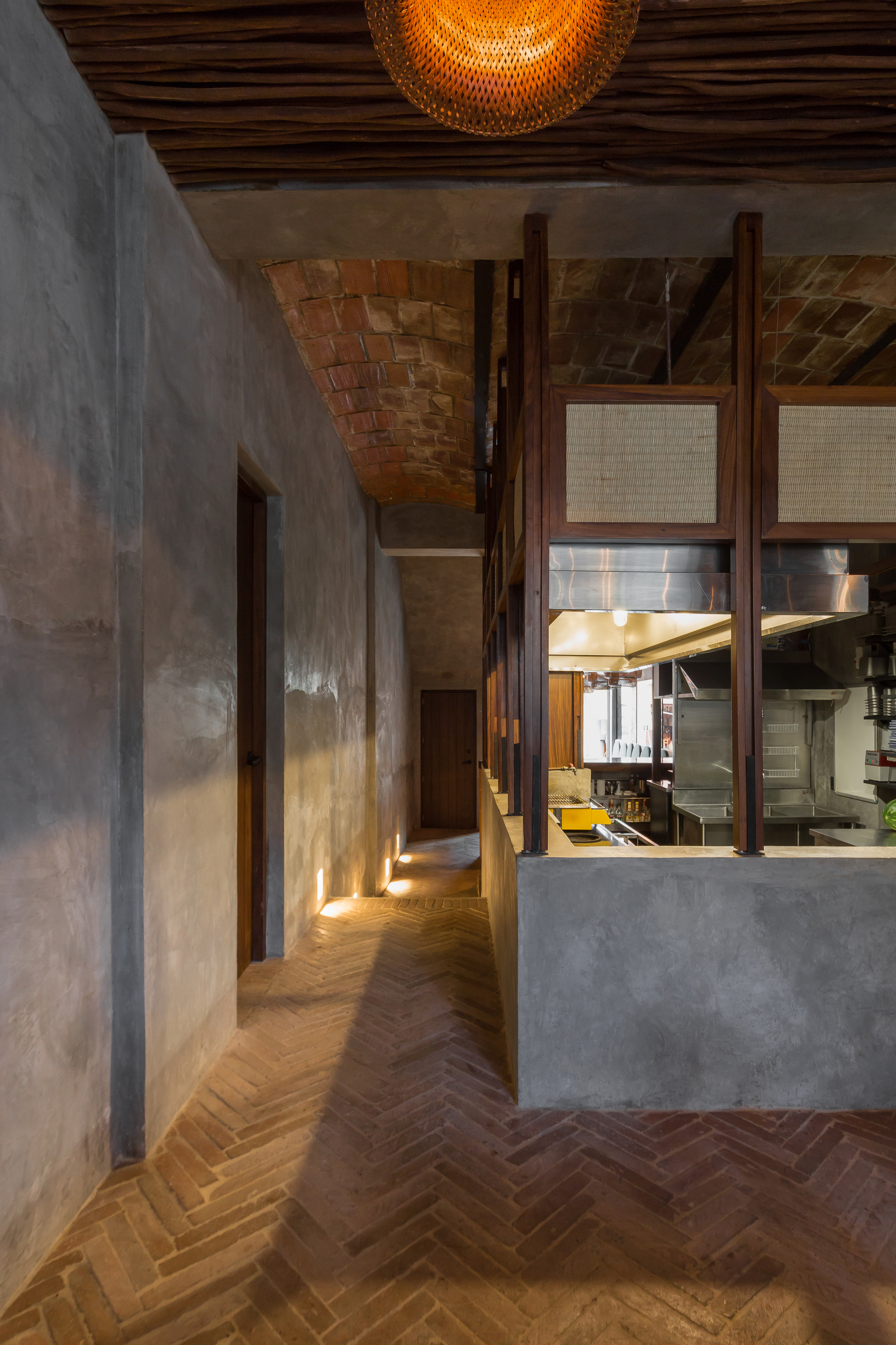 Herringbone brick floor leading past the plastered kitchen block toward a brick vaulted ceiling, with low lights along the wall