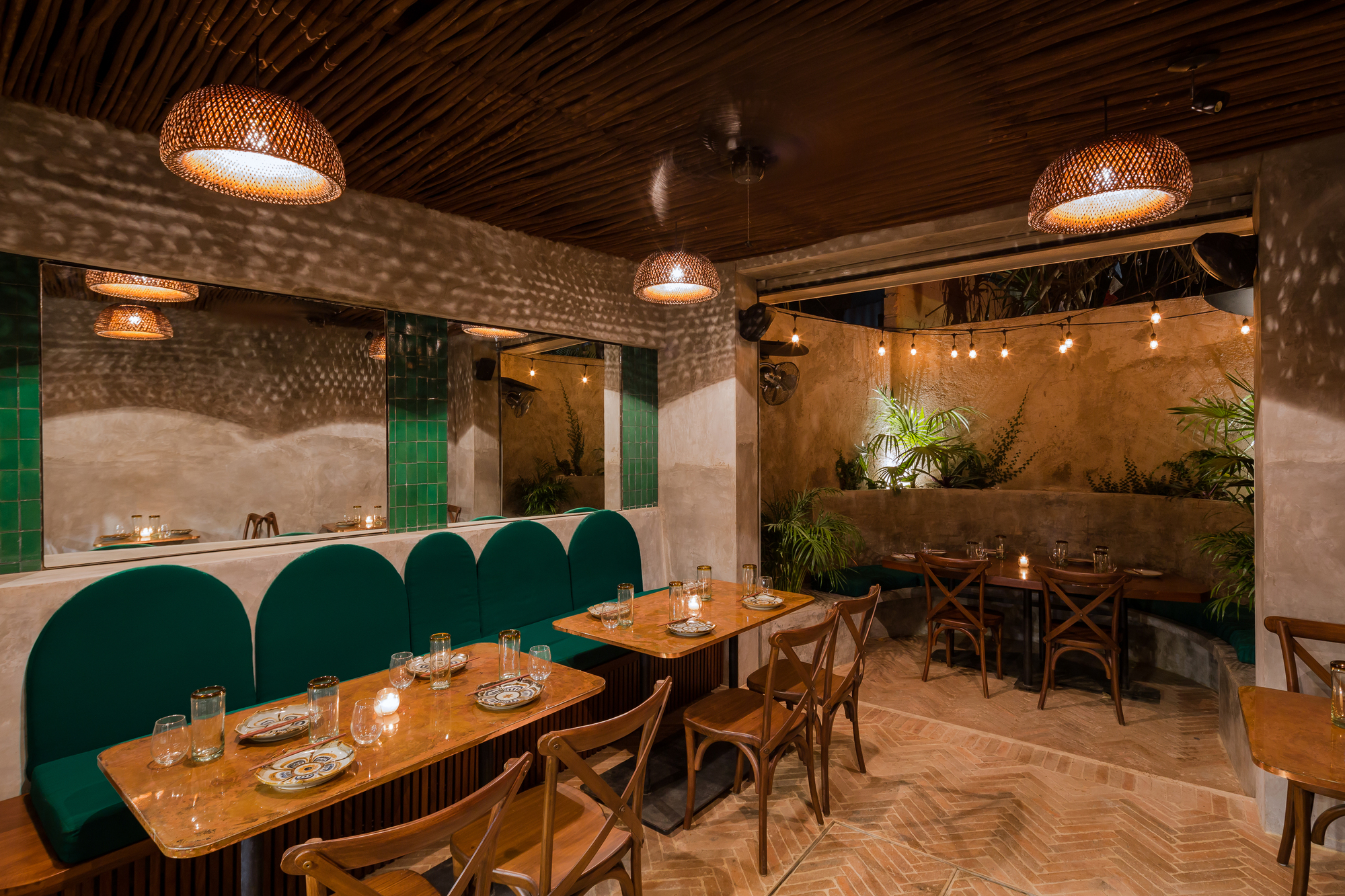 Evening dining area with arched green banquette, mirror panels and string lights over a planted patio corner