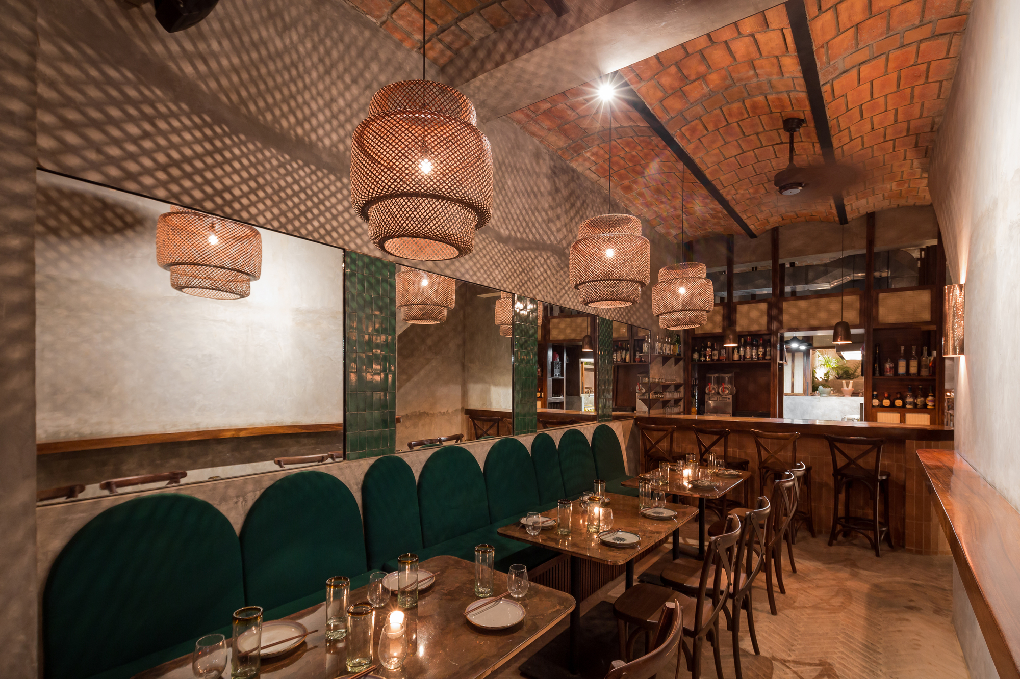 Dining room with green arched banquettes, woven pendant lamps and a brick vaulted ceiling lit warmly at night