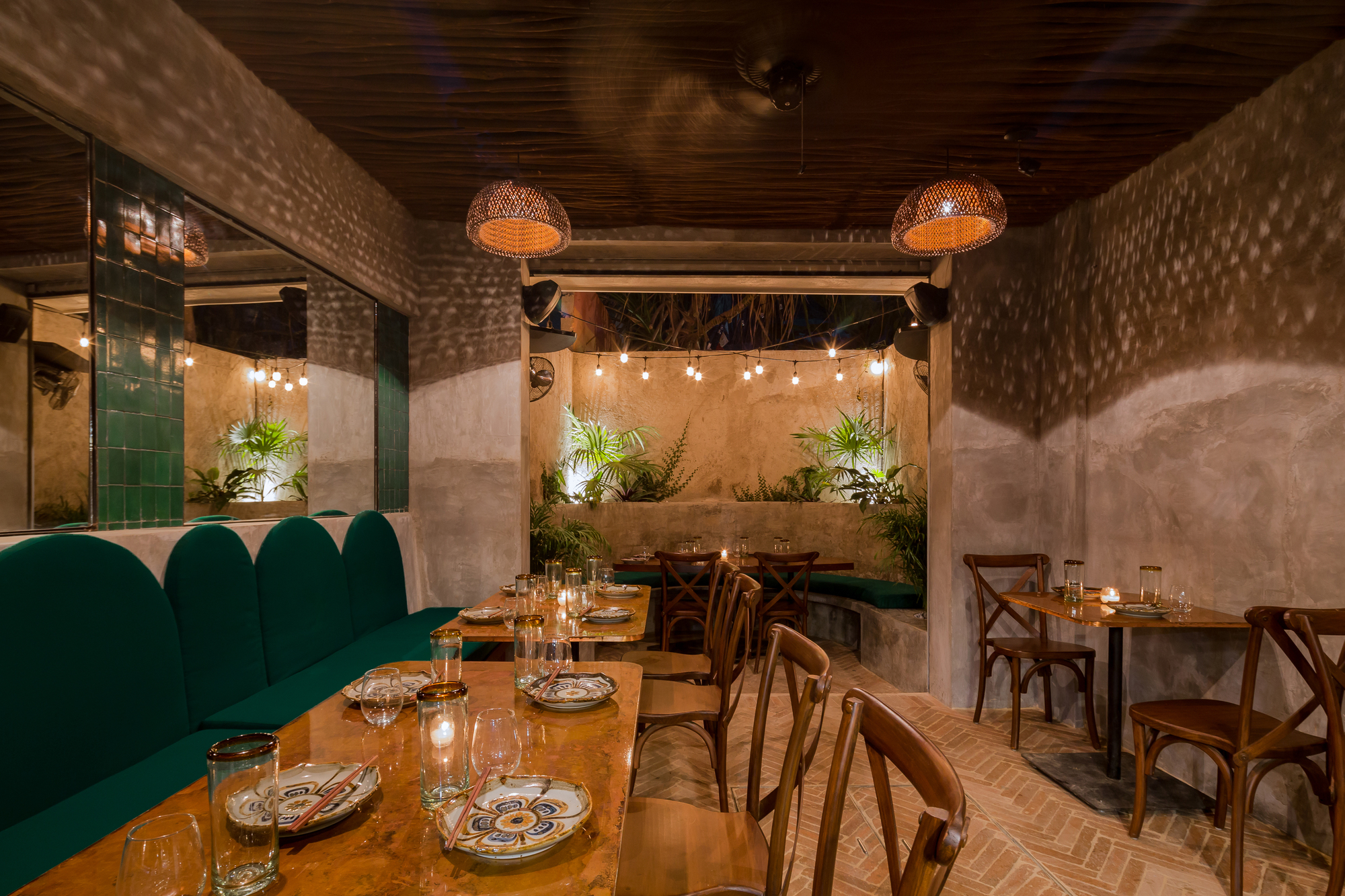 Dining area with green banquette, mirrored wall and string lights over a planted courtyard glimpsed at the far end at night
