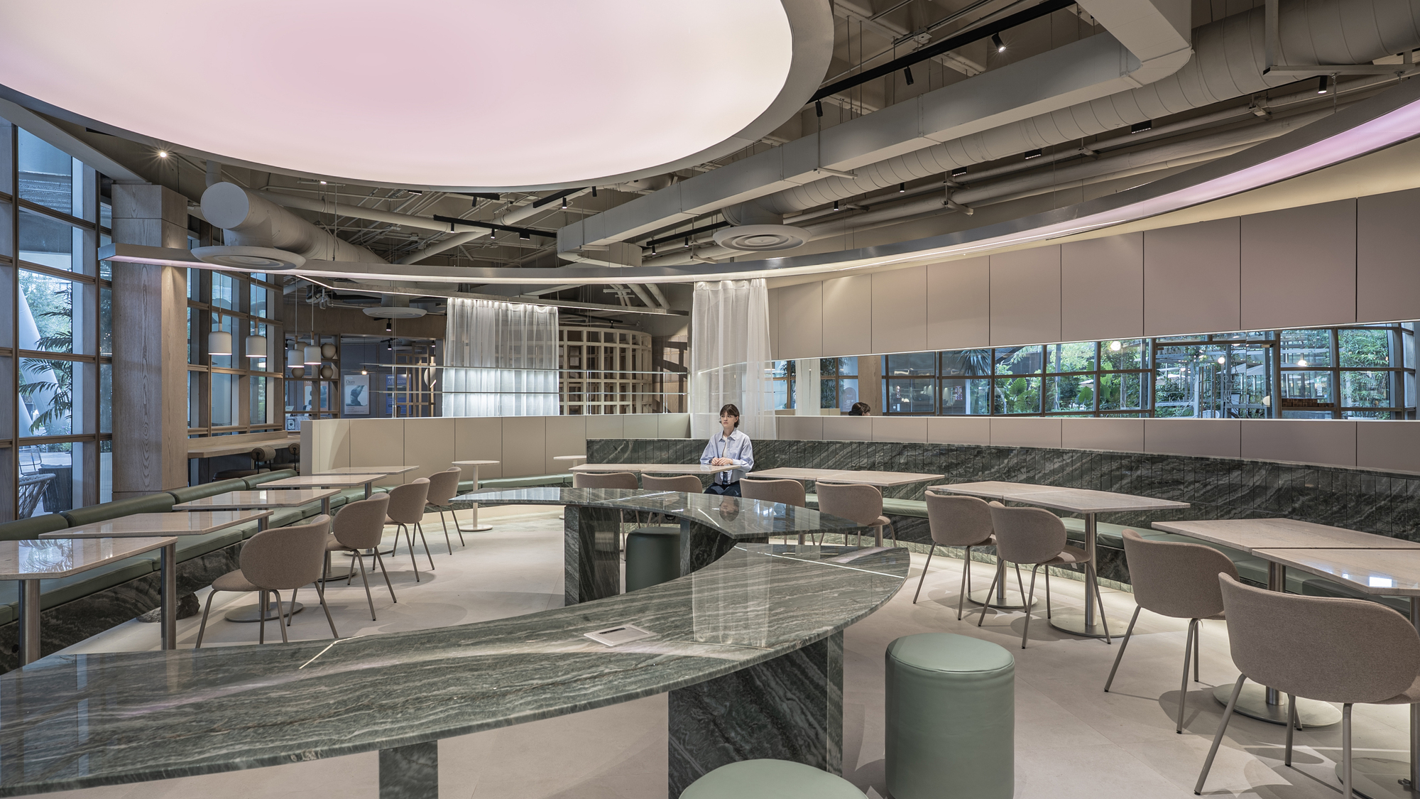 Curved green marble counter in the foreground with round stools, taupe chairs and a glowing pink oval ceiling above a seated diner