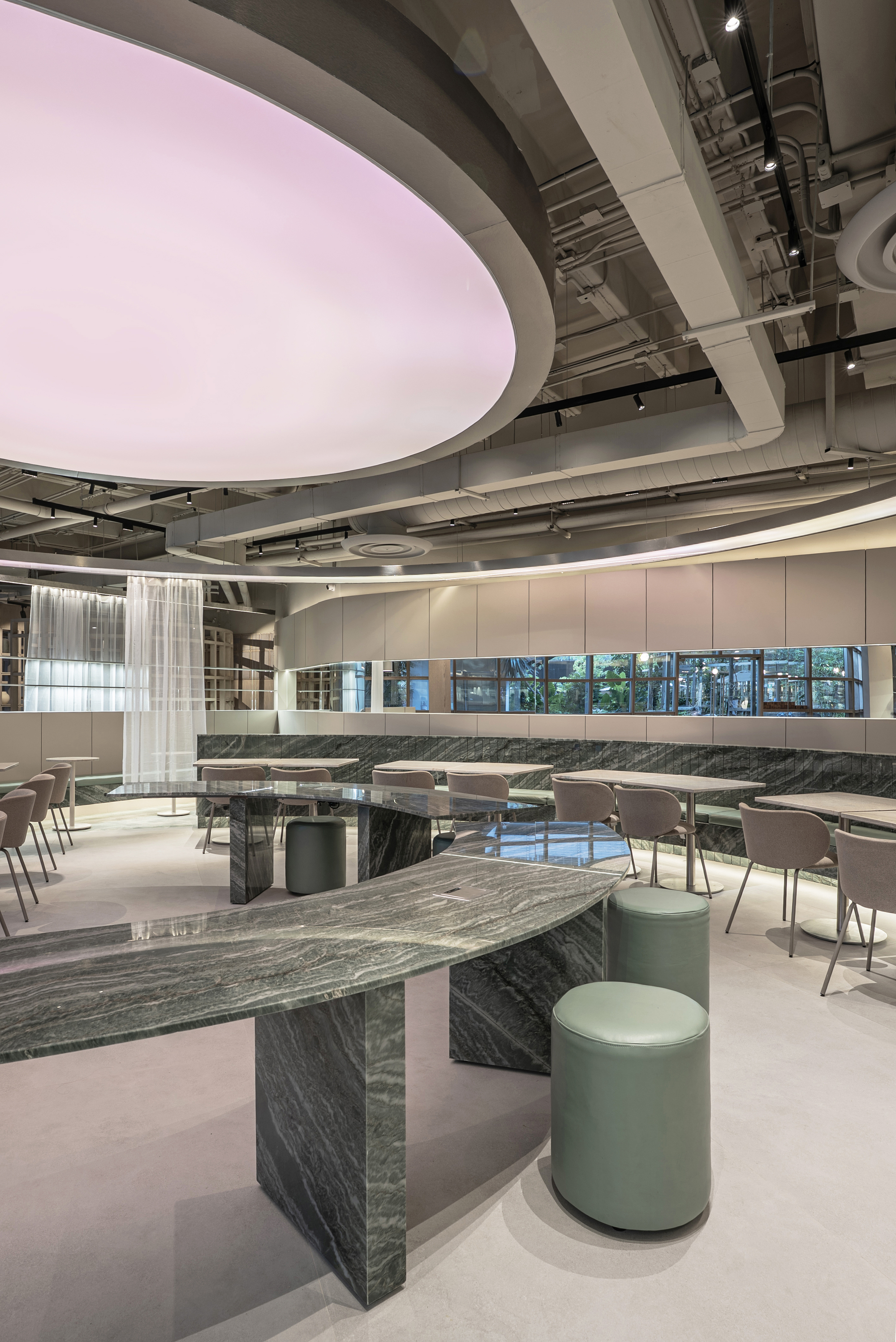 Green leather stools beside a sloping marble counter, with a pink ceiling disc and garden-facing windows in the background