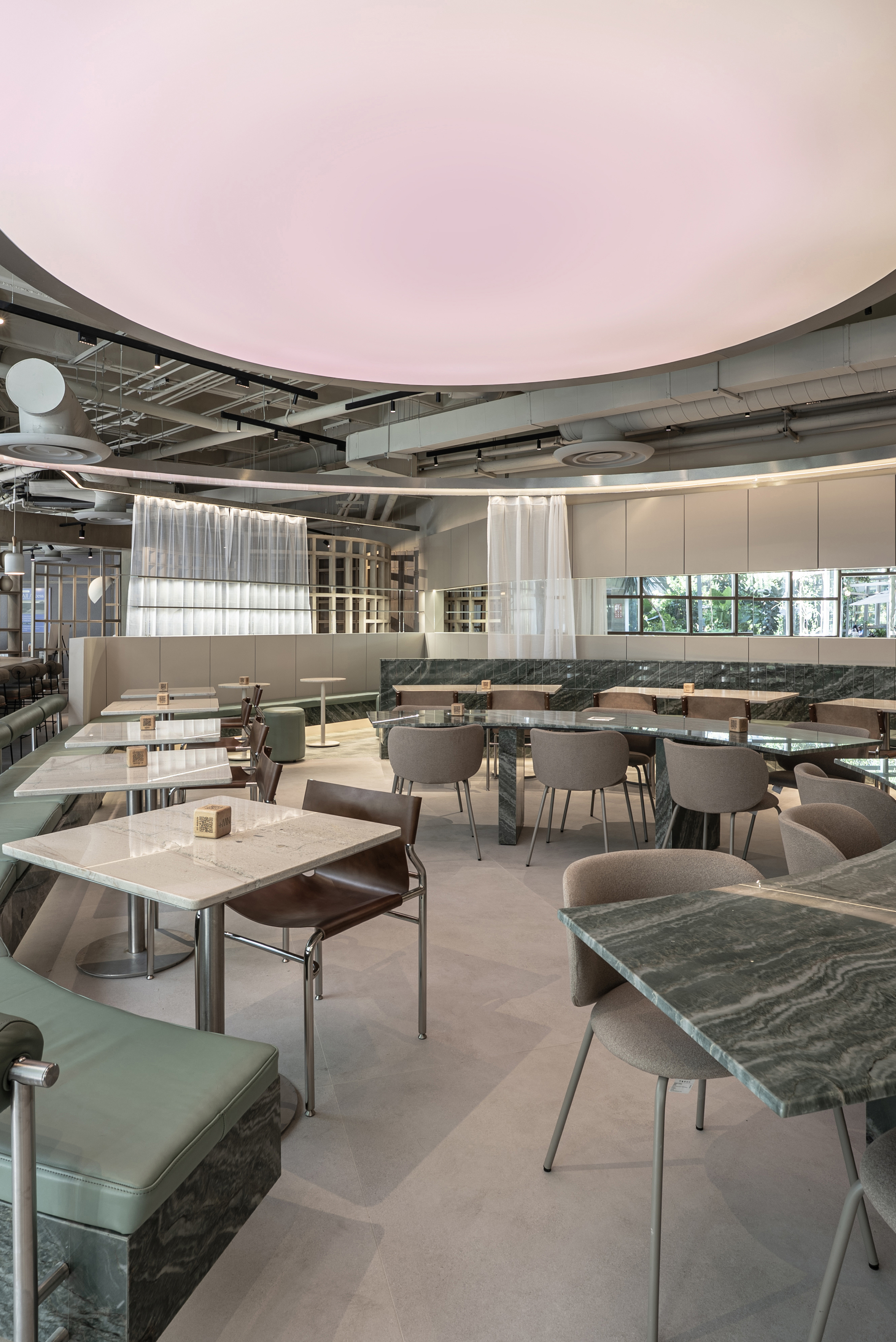 Marble-topped tables and taupe chairs under the pink ceiling disc, with sheer curtains hanging beside the mirrored wall band