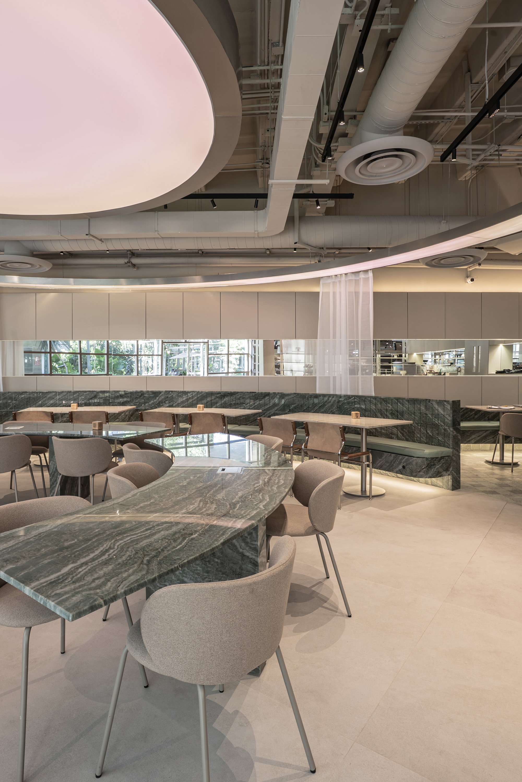Veined green marble table in the foreground with a pink-lit oval ceiling and exposed ductwork overhead