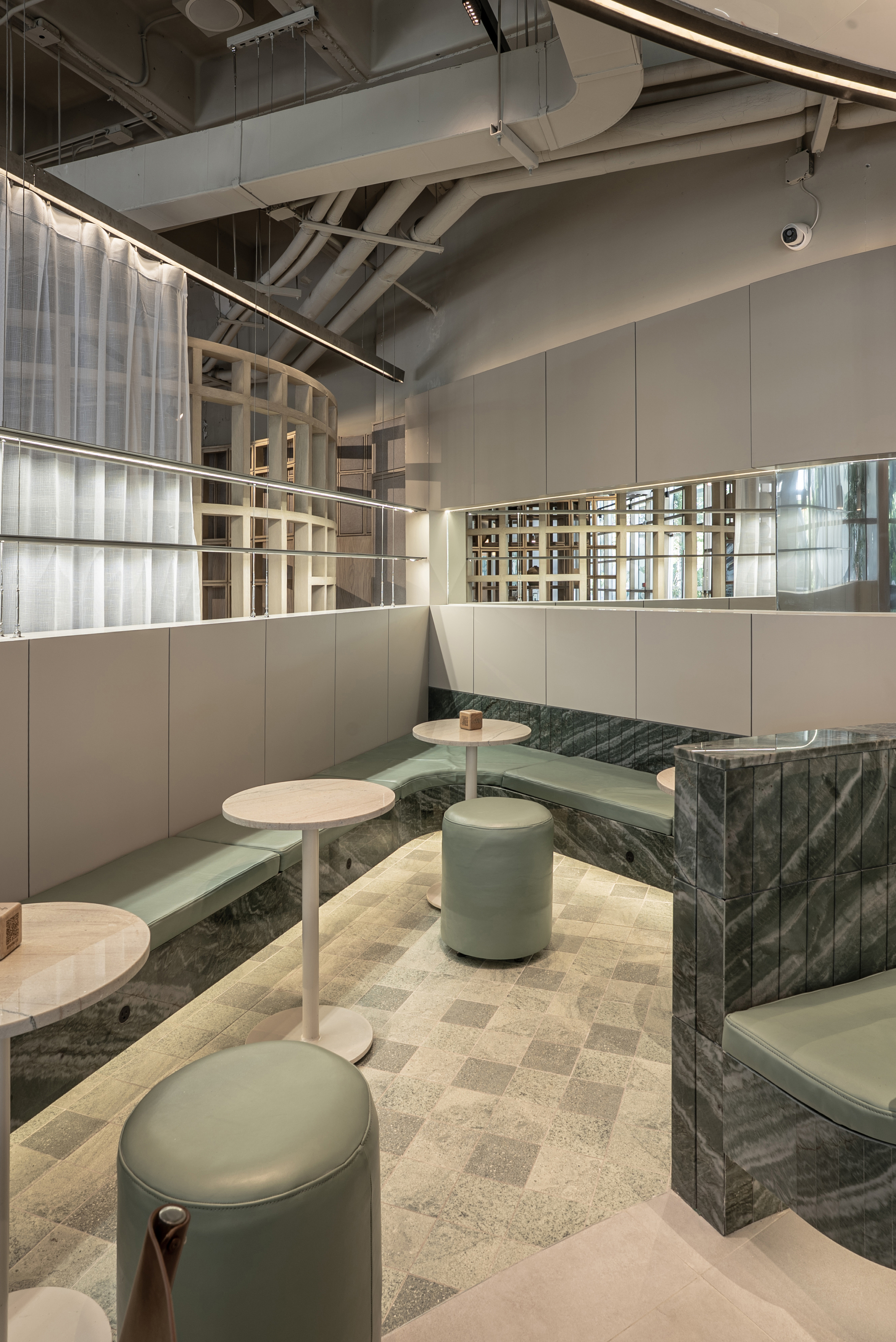 Corner banquette with sage leather cushions, green stone cladding and round stools on a mosaic stone floor beneath exposed ductwork