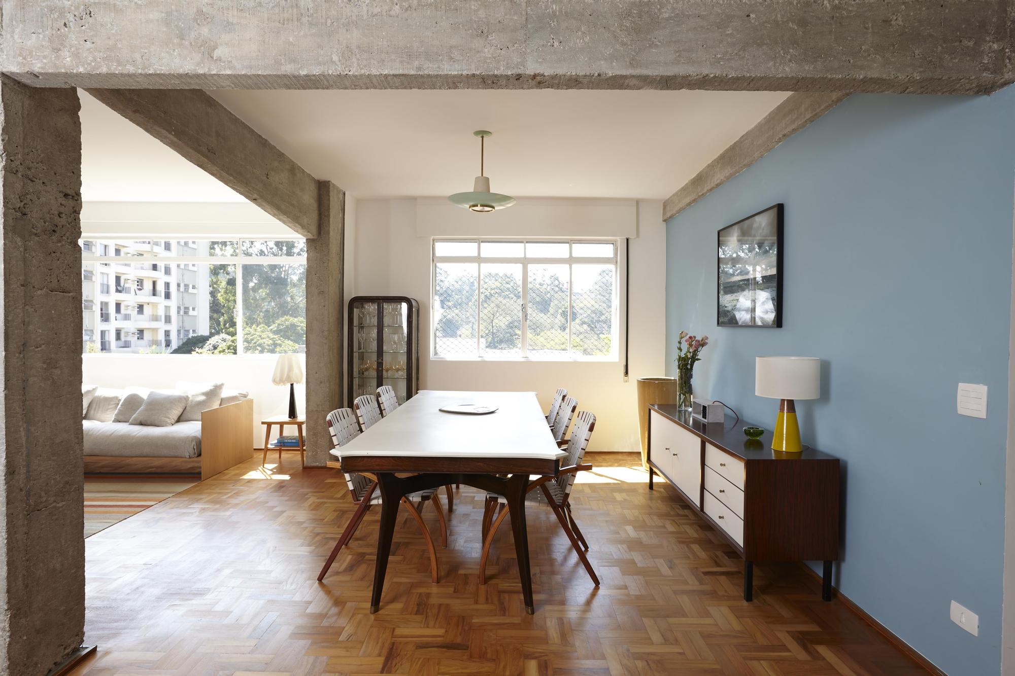 Dining table and blue painted wall seen through a concrete frame, with sunlight falling across the herringbone parquet floor