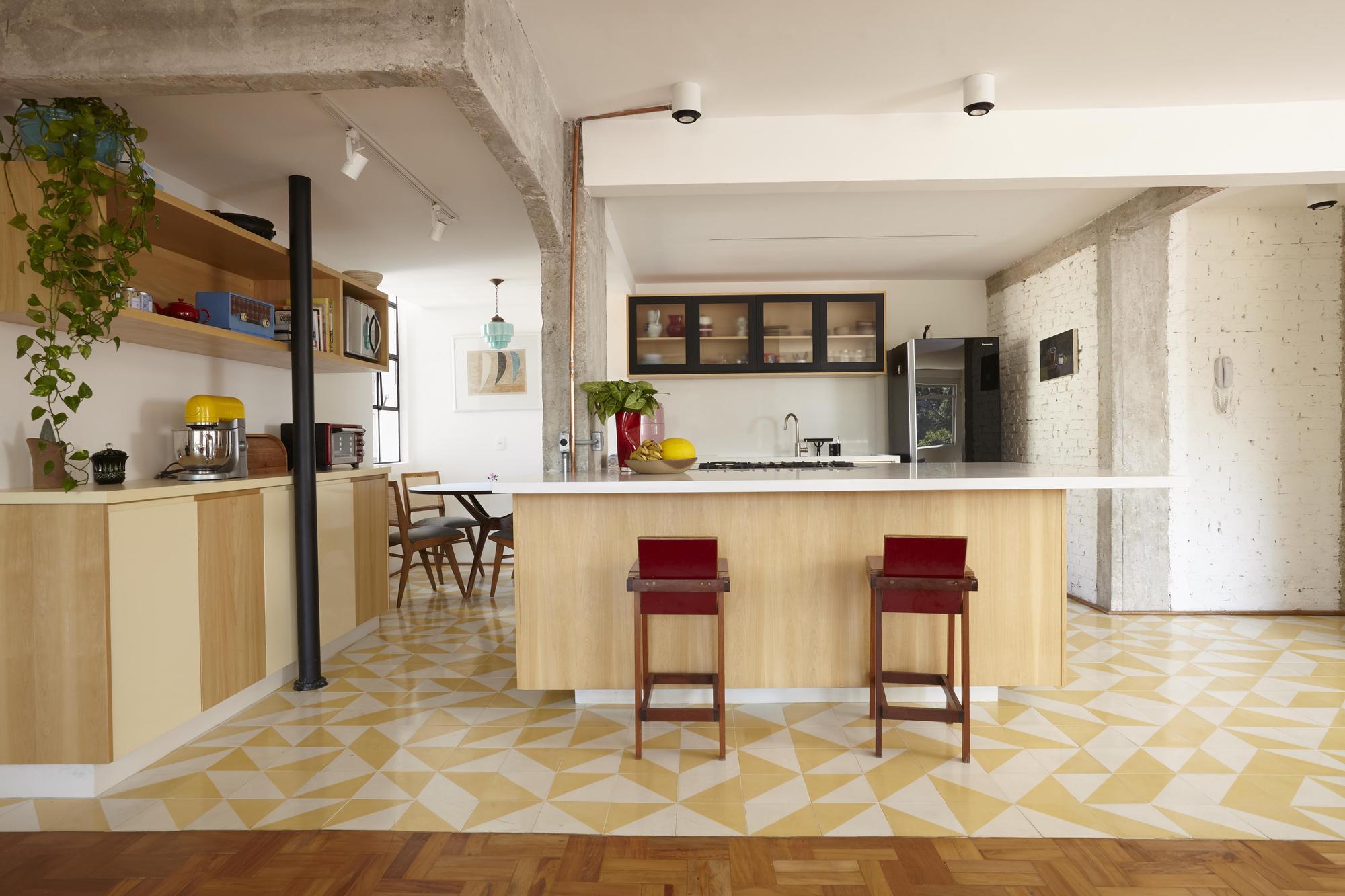 Kitchen island in pale wood with two red-seated stools on yellow and white triangle tile, beside a painted brick wall