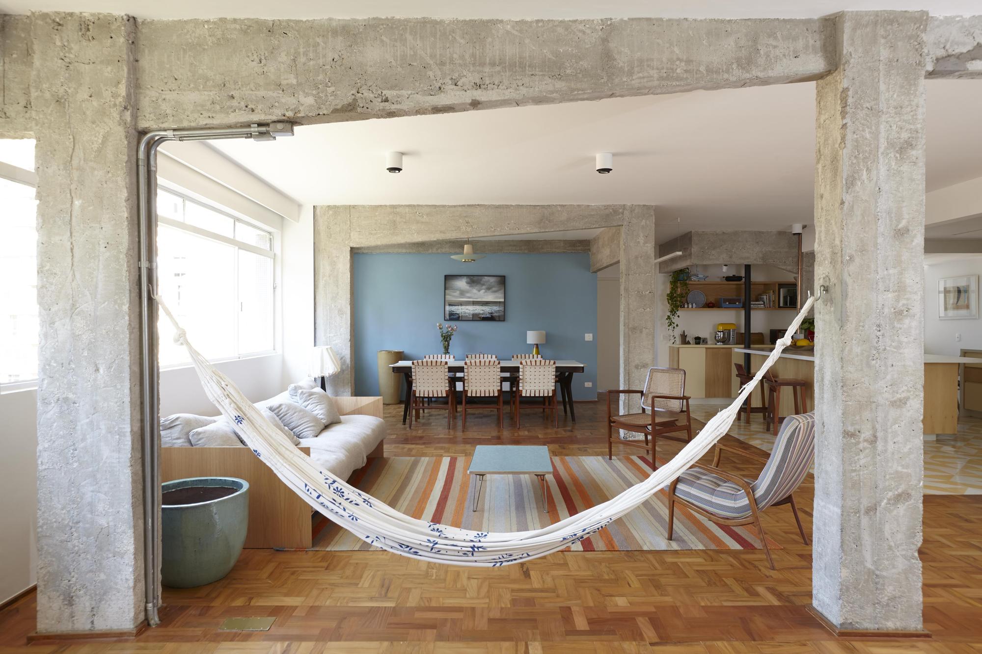 Hammock slung between two board-marked concrete columns, with the blue-walled dining area and kitchen visible in the daylight beyond