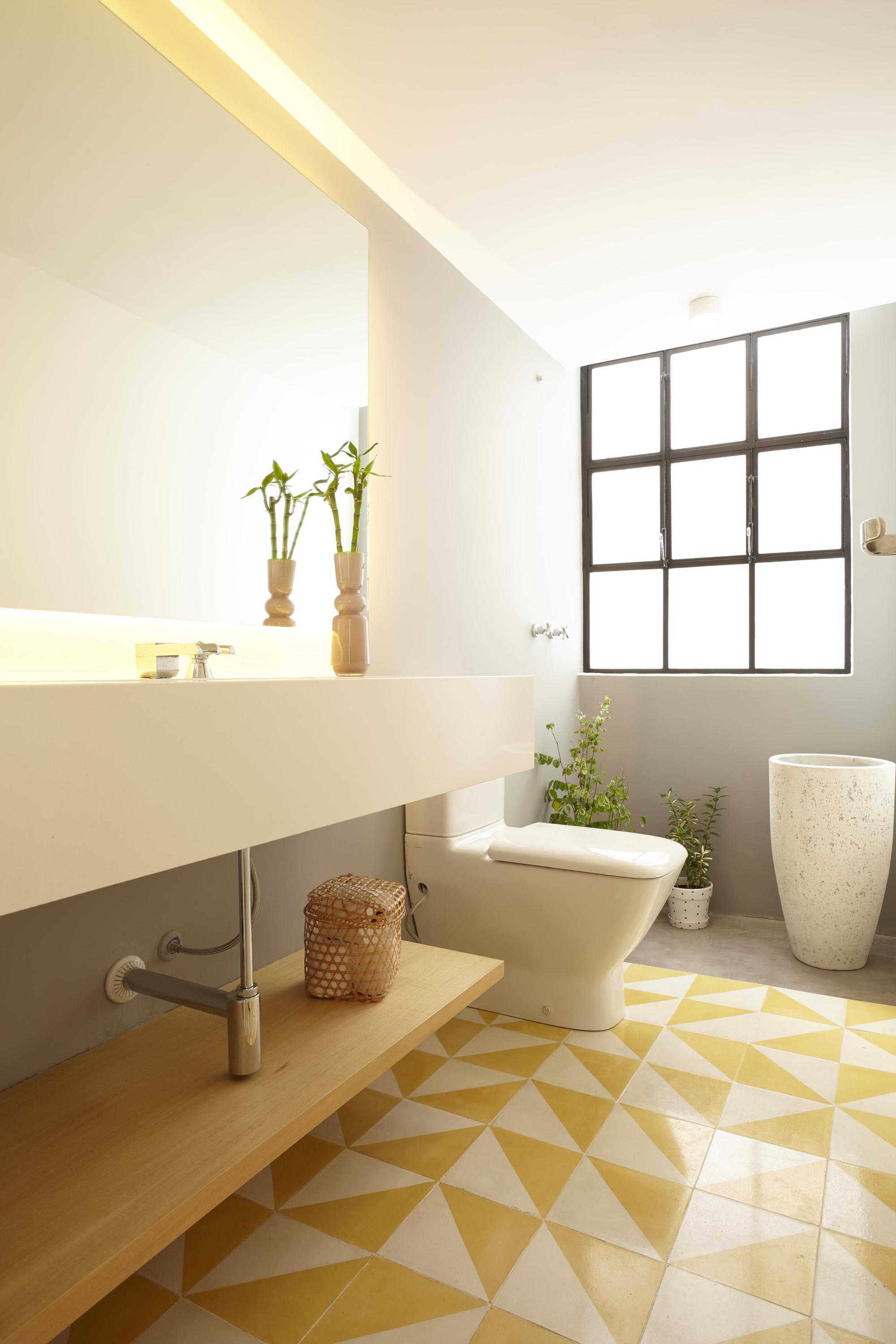 Bathroom with a floating white basin counter, yellow triangle floor tile and a steel-framed window, with bamboo stalks and potted plants