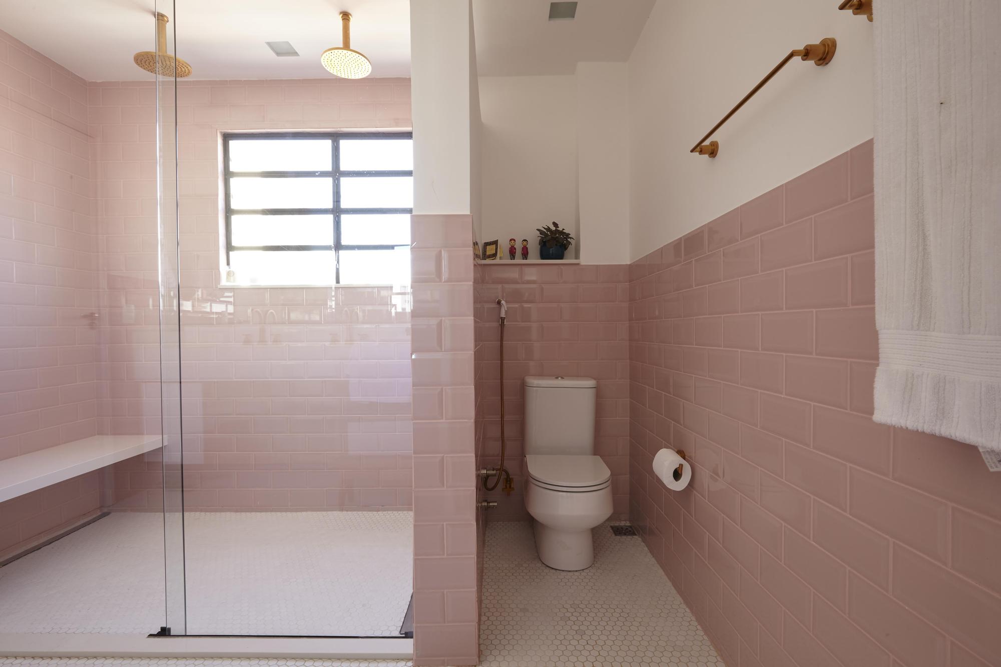 Pink subway tile bathroom with a glass-enclosed walk-in shower, brass rain showerheads and a toilet, lit by a steel-framed window