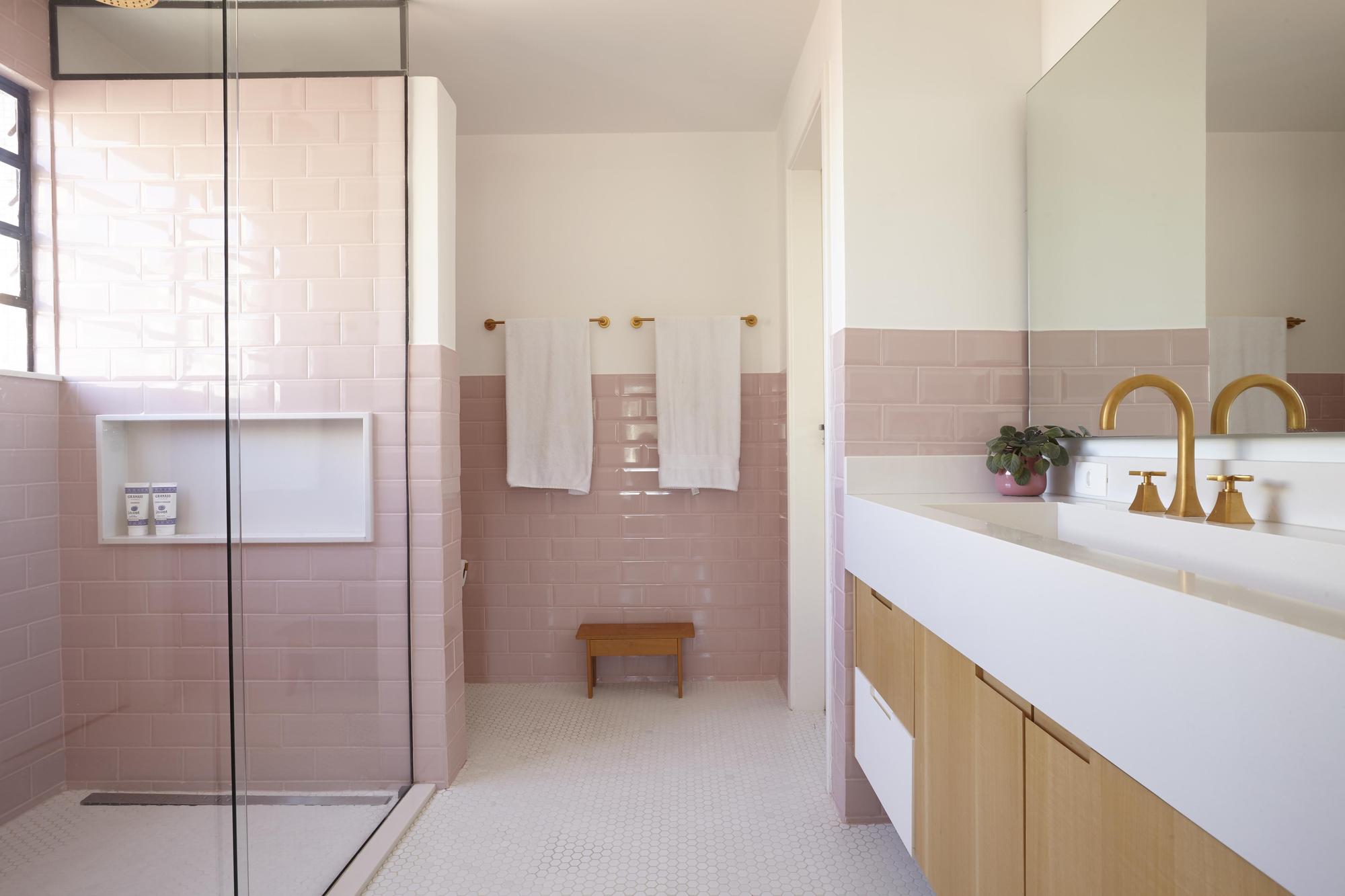 Bathroom with pink subway tile walls, glass shower screen, brass faucets and a light wood vanity under soft daylight
