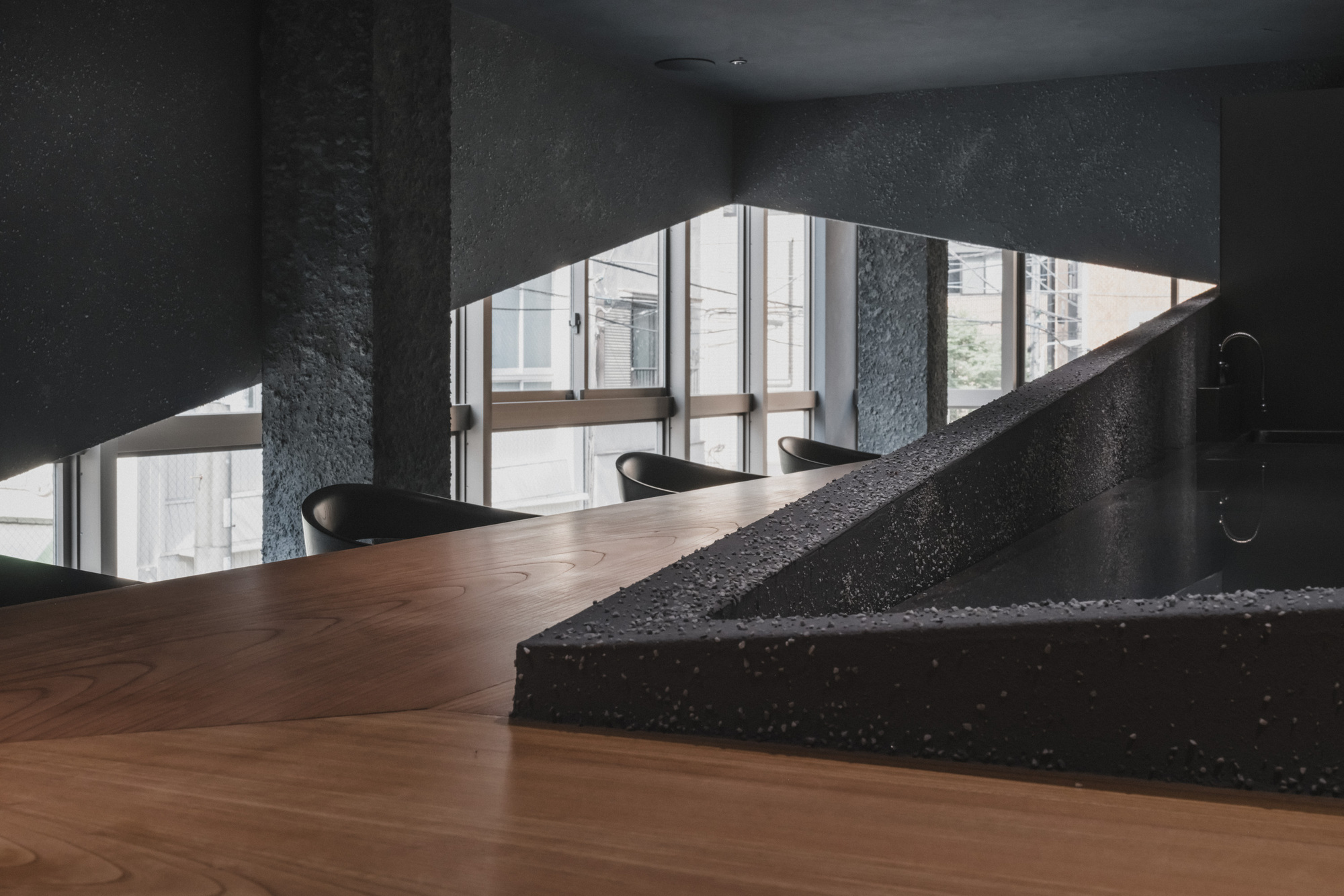 Wood counter top with grain in the foreground and a pebble-studded dark kitchen edge, set against windows with daylight