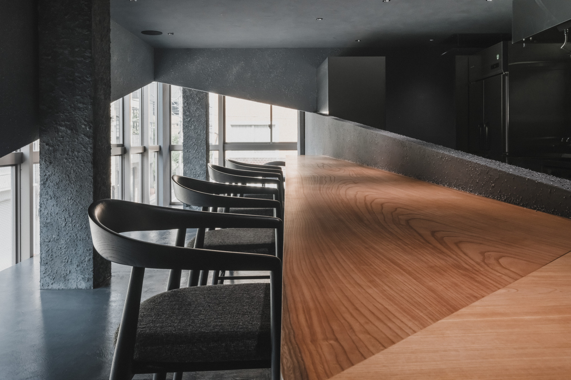 Close view of the figured wood counter top and charcoal armchair stools, with sunlit windows and a rough column behind