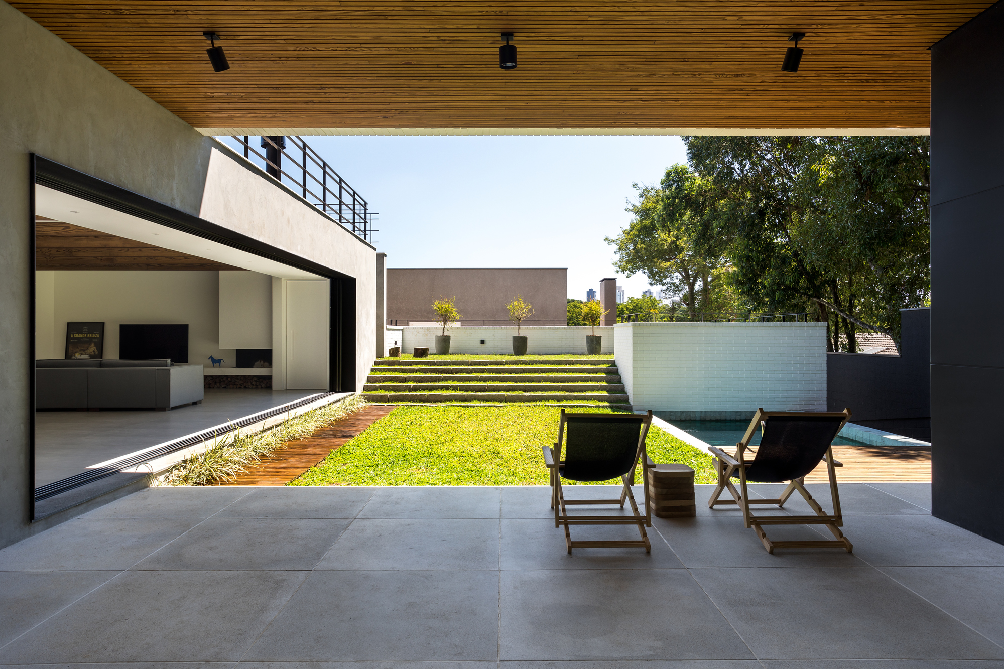 View from a covered terrace with two folding chairs facing a lawn, grass steps and a white brick wall beside the pool