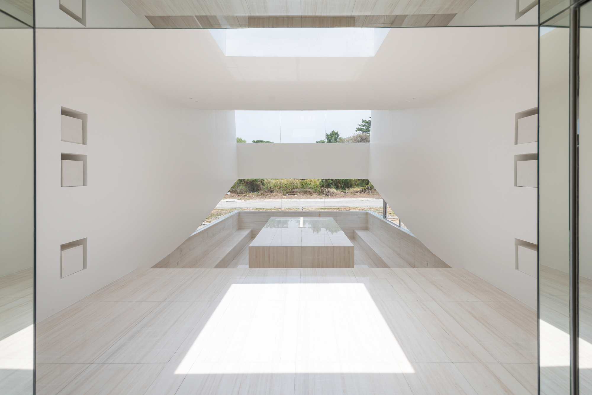 Interior of the pale stone chapel with a central block, stepped seating and a patch of sunlight on the floor