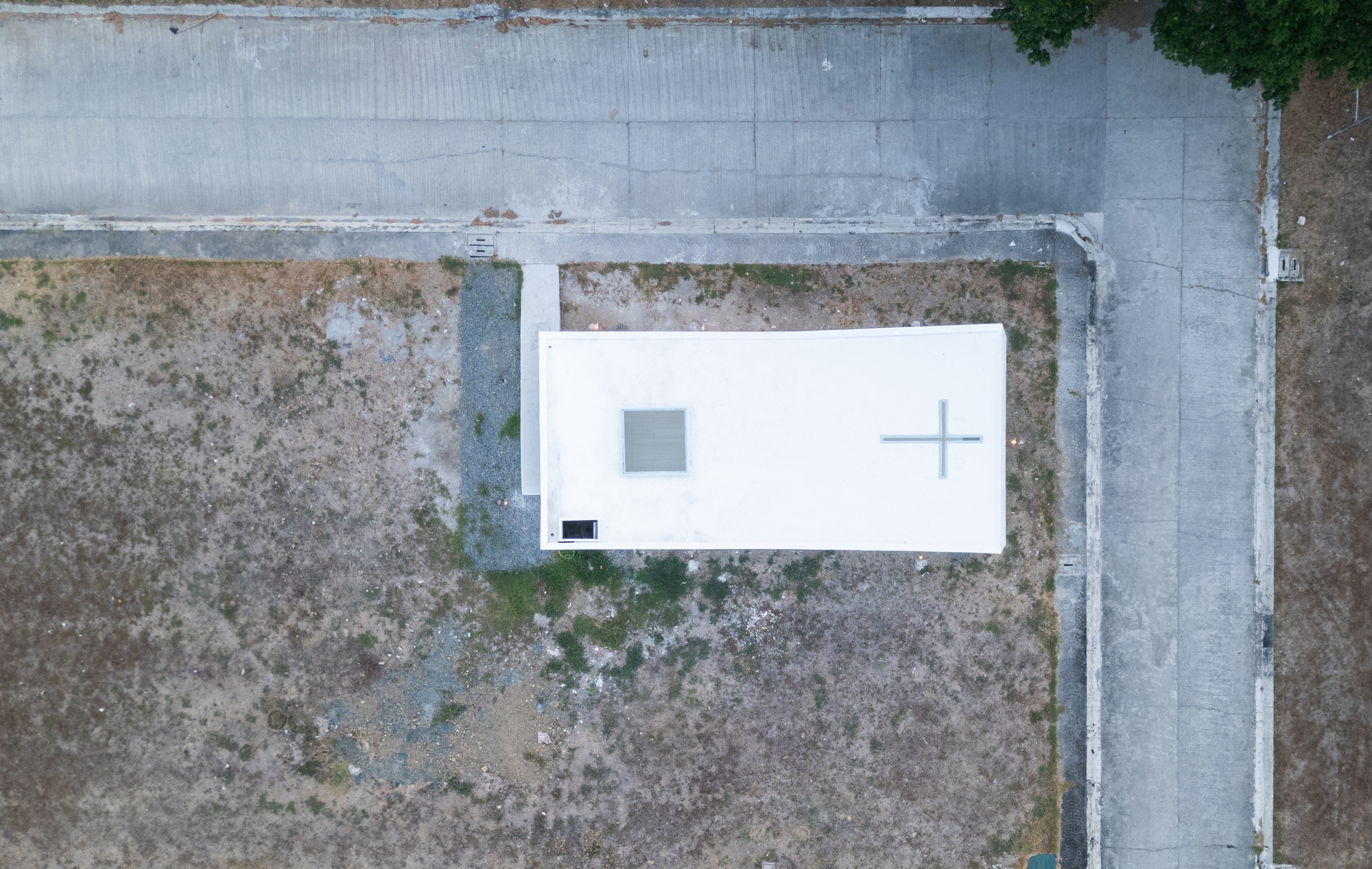 Top-down drone view of the white rectangular roof with a square skylight and cross cut-out on a dry lot beside concrete roads