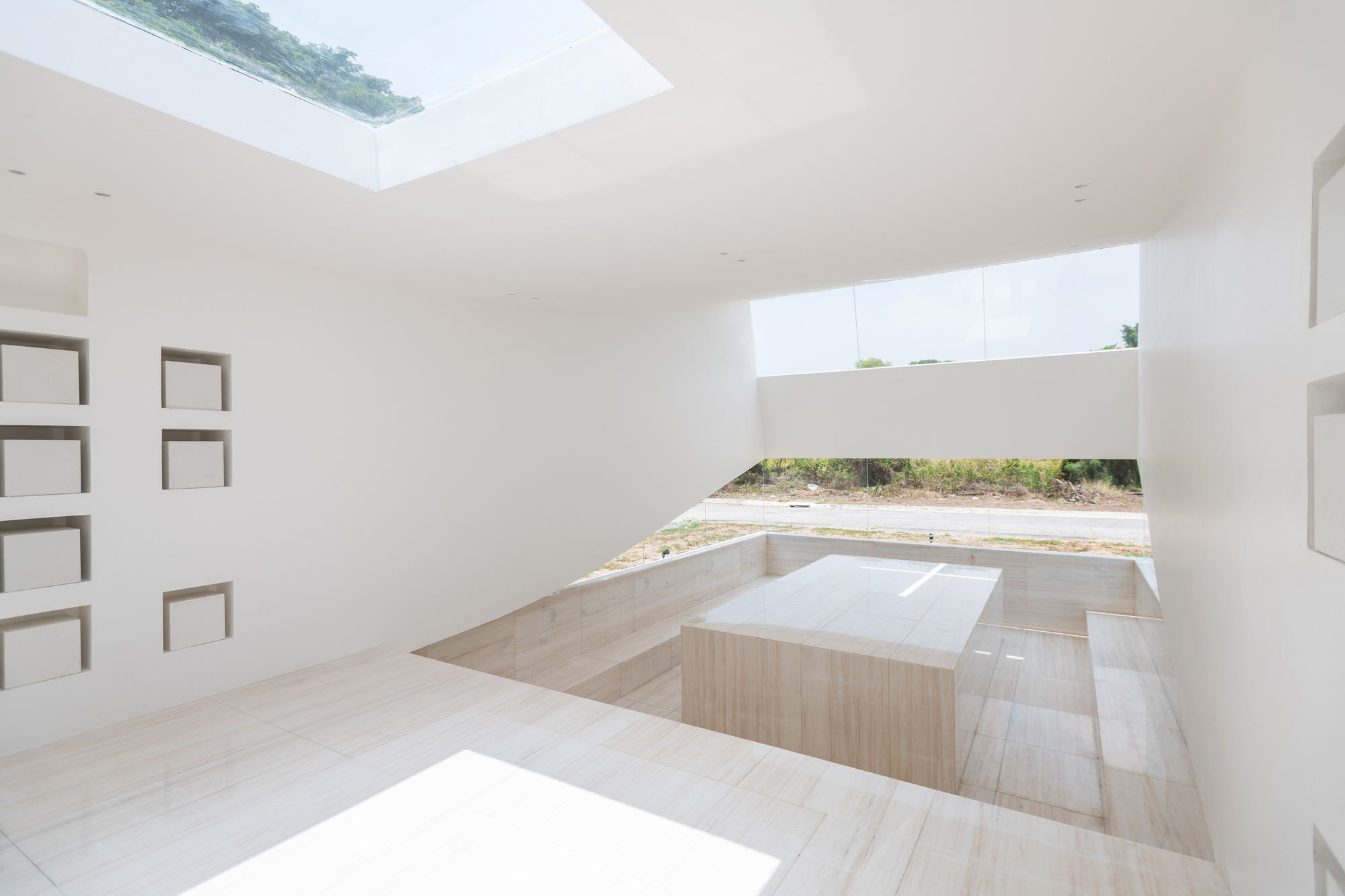 Interior with a stone altar block in a sunken travertine pit, niches on the left wall and a skylight overhead