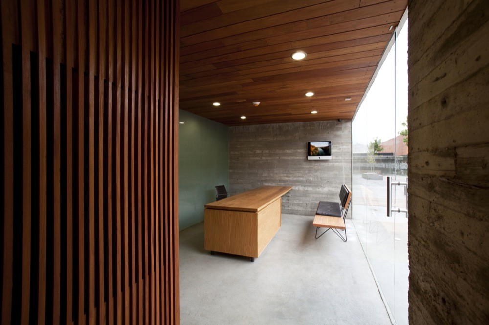 Reception room with a wood desk, slatted timber screen and glass wall, under a slatted timber ceiling in soft daylight