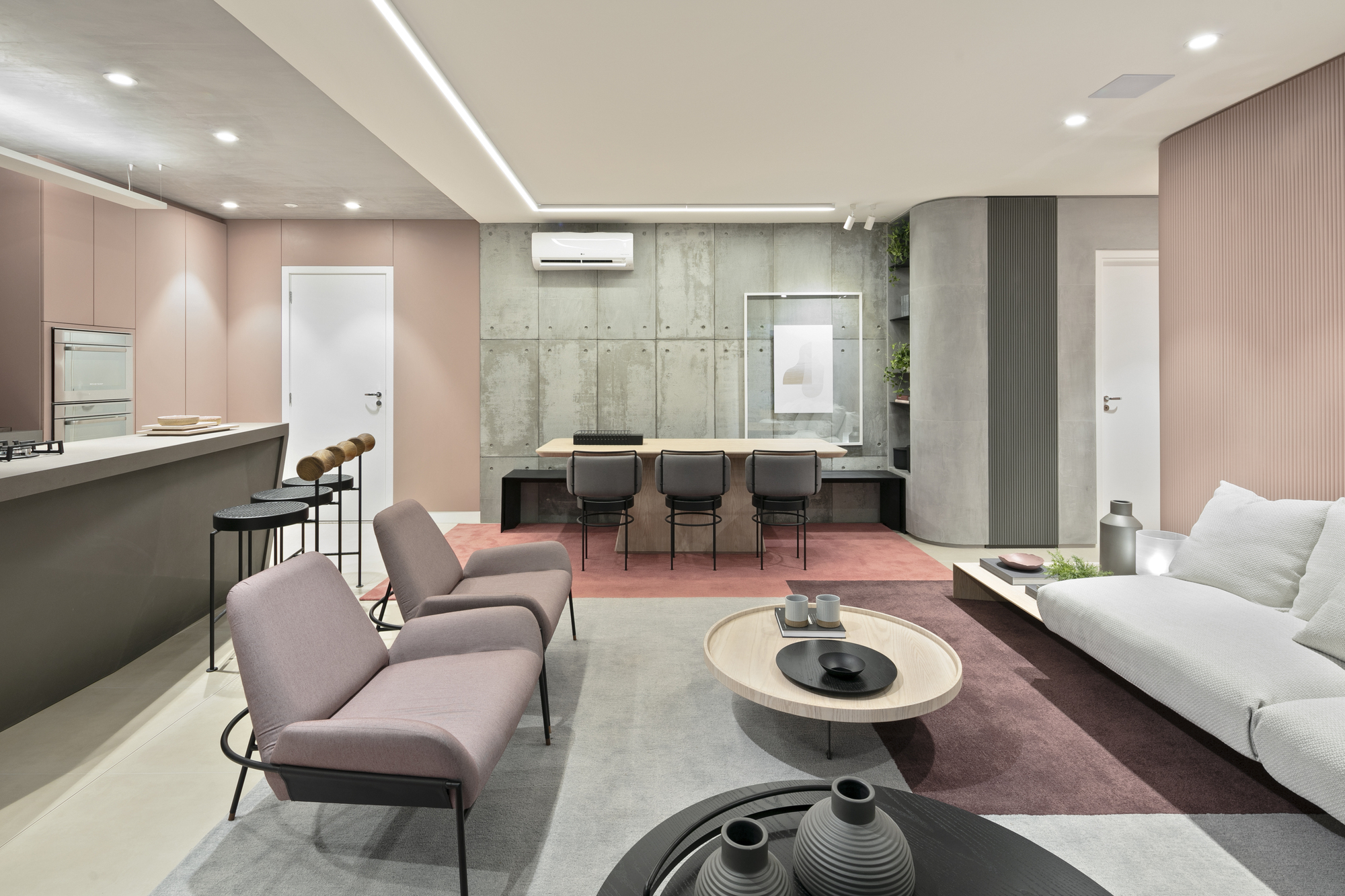 View across the lounge toward a concrete wall and dining table, with mauve armchairs and a round wood coffee table in the foreground