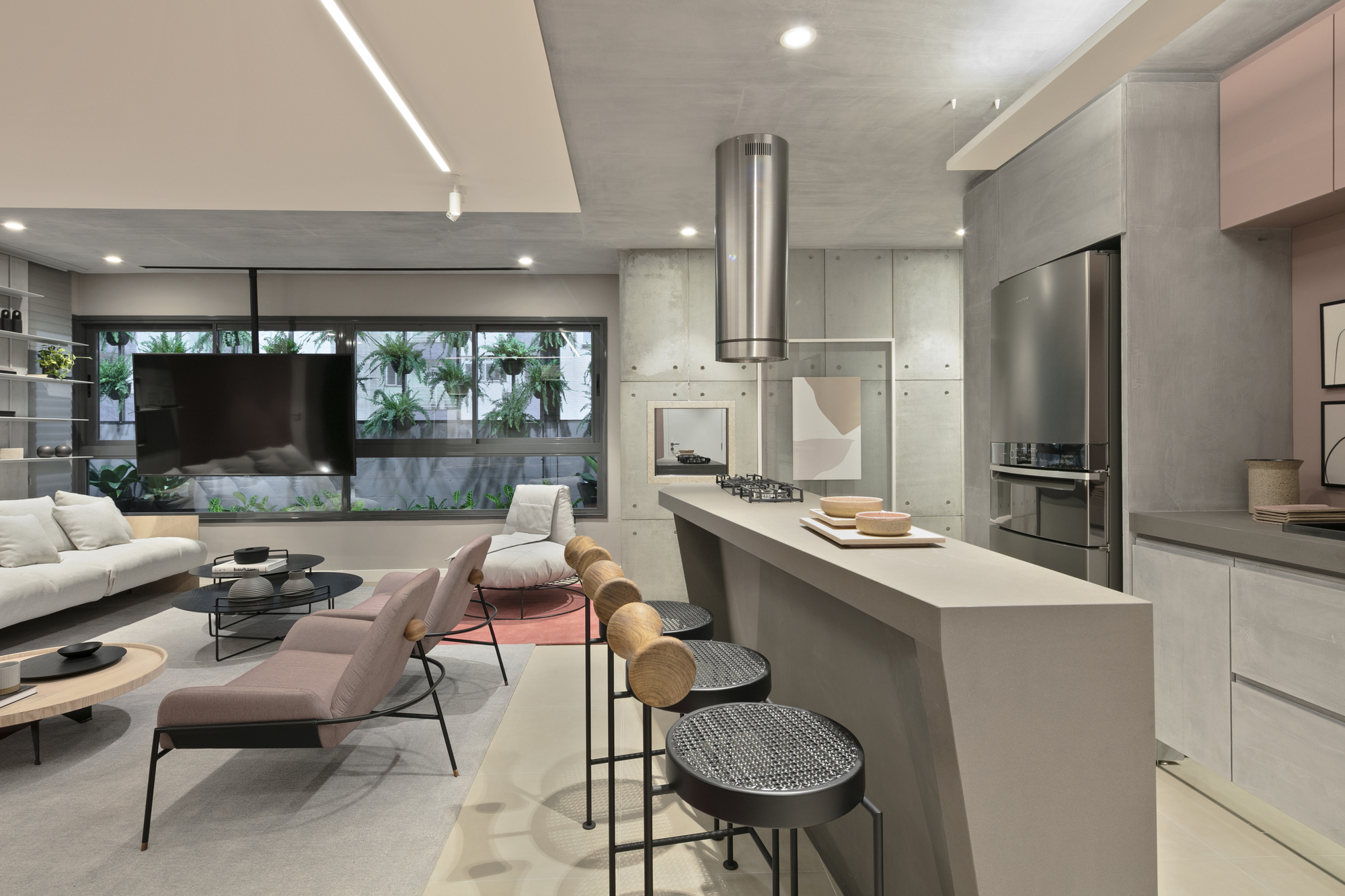 Angular concrete kitchen island with woven black stools, facing a window wall onto a planted courtyard in daylight