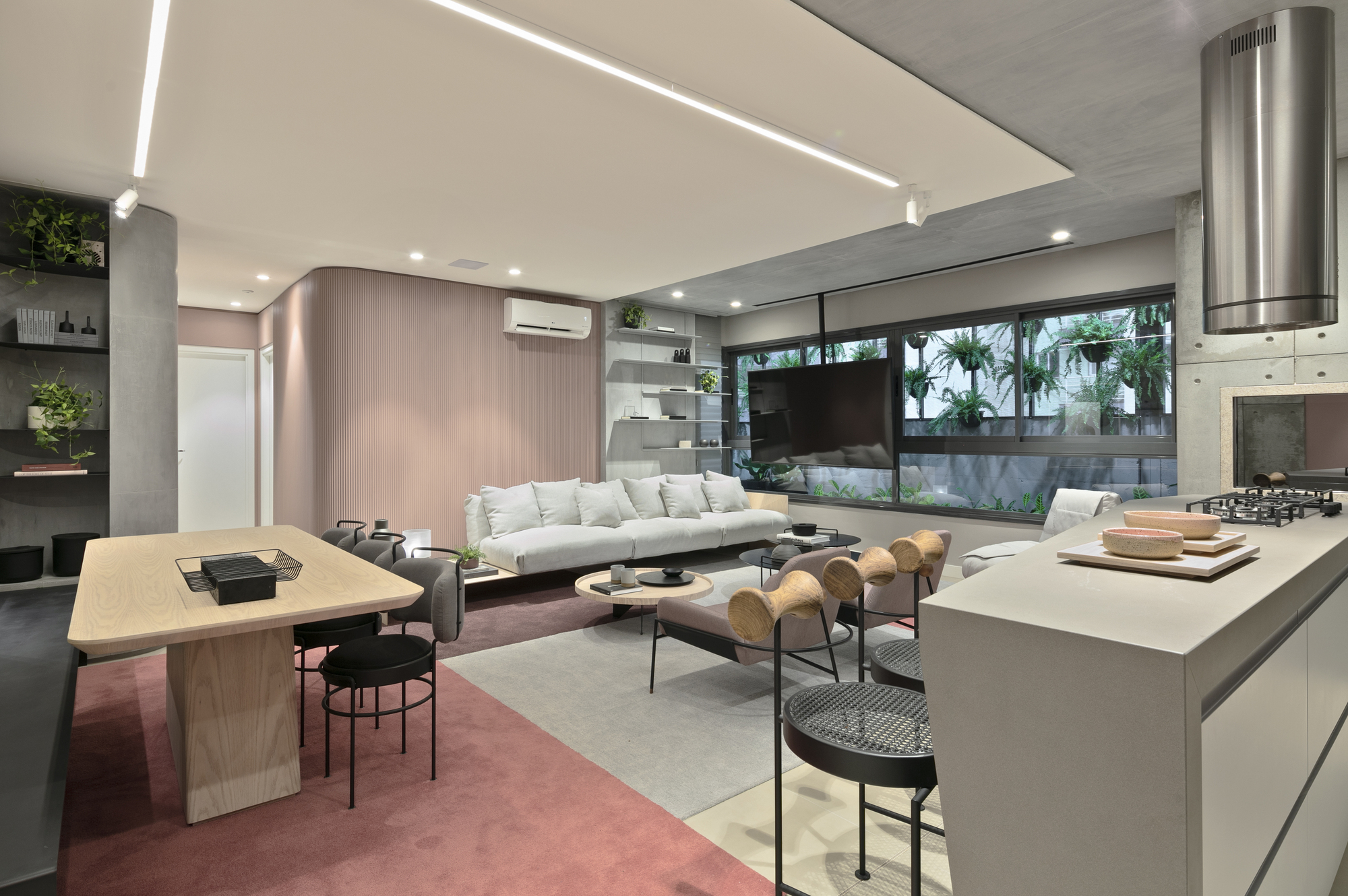 Open plan interior linking a timber dining table, the sofa area and a concrete kitchen island under linear ceiling lights