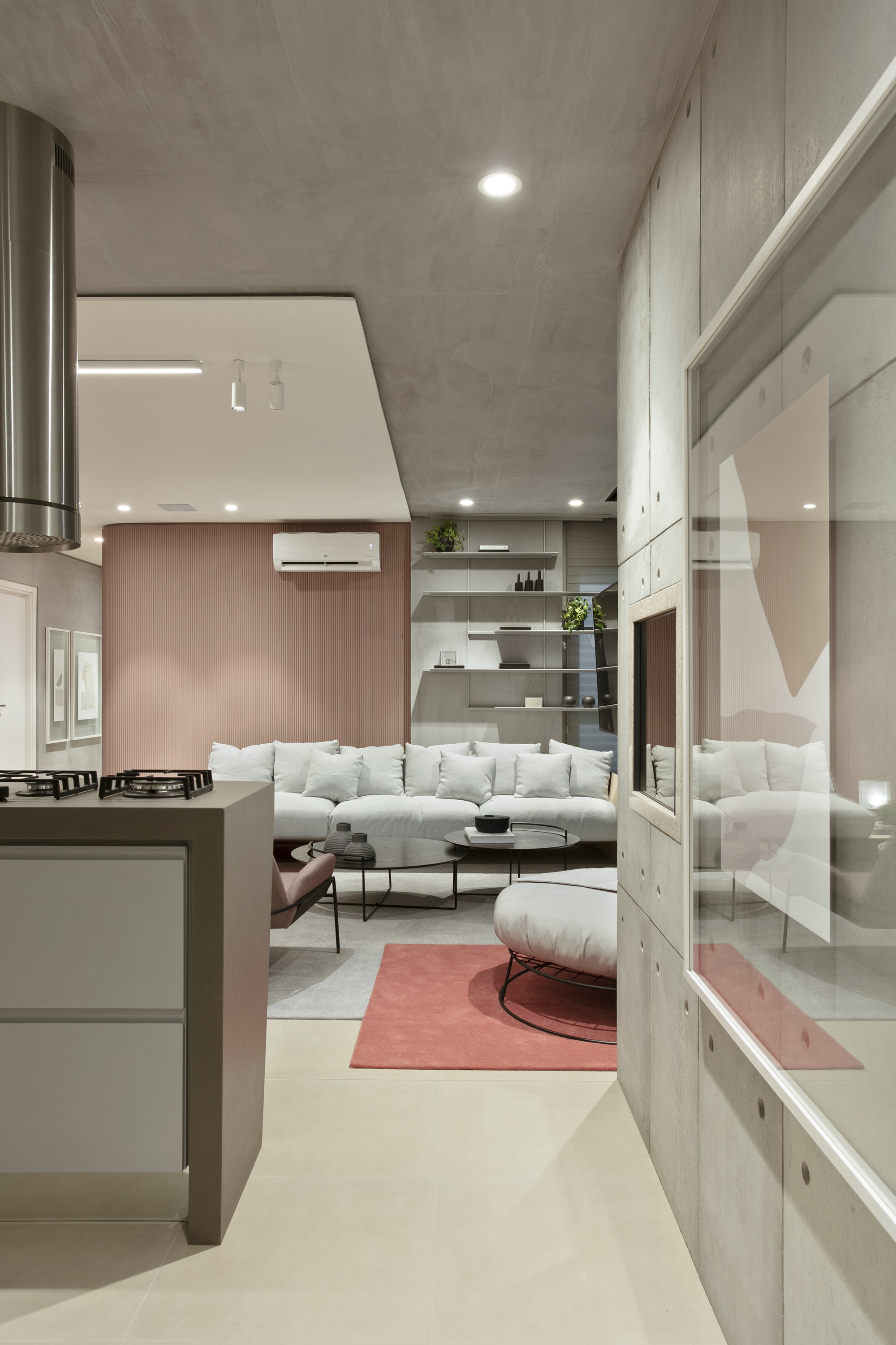 View past the kitchen island and concrete-panel wall toward the sofa, with a coral rug on the pale floor