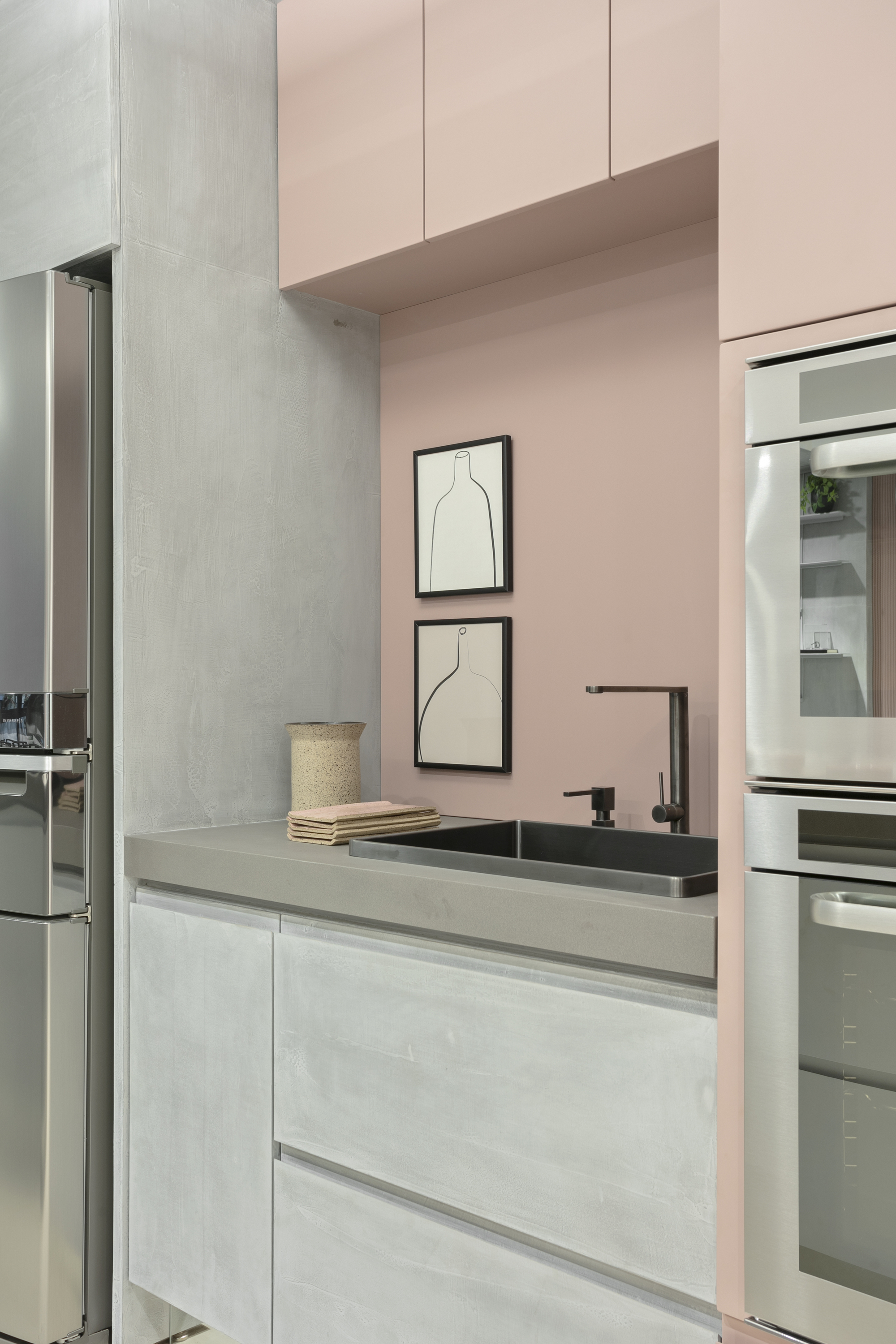 Kitchen corner with a black sink and tap, two framed vase prints on a pink wall and steel ovens