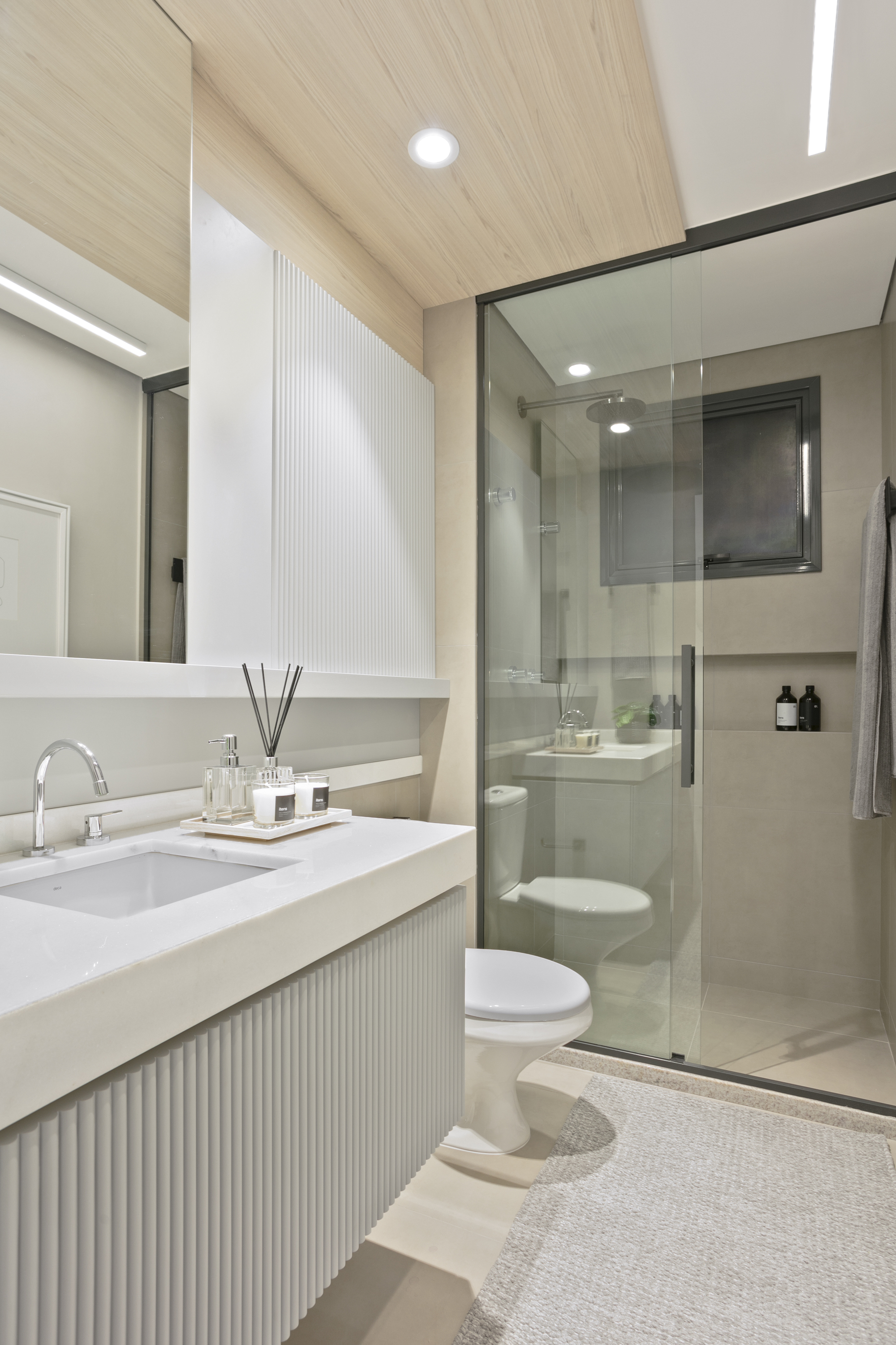 Bathroom with a fluted white vanity, undermount sink, glass shower enclosure and a wood-look ceiling lit by round downlights