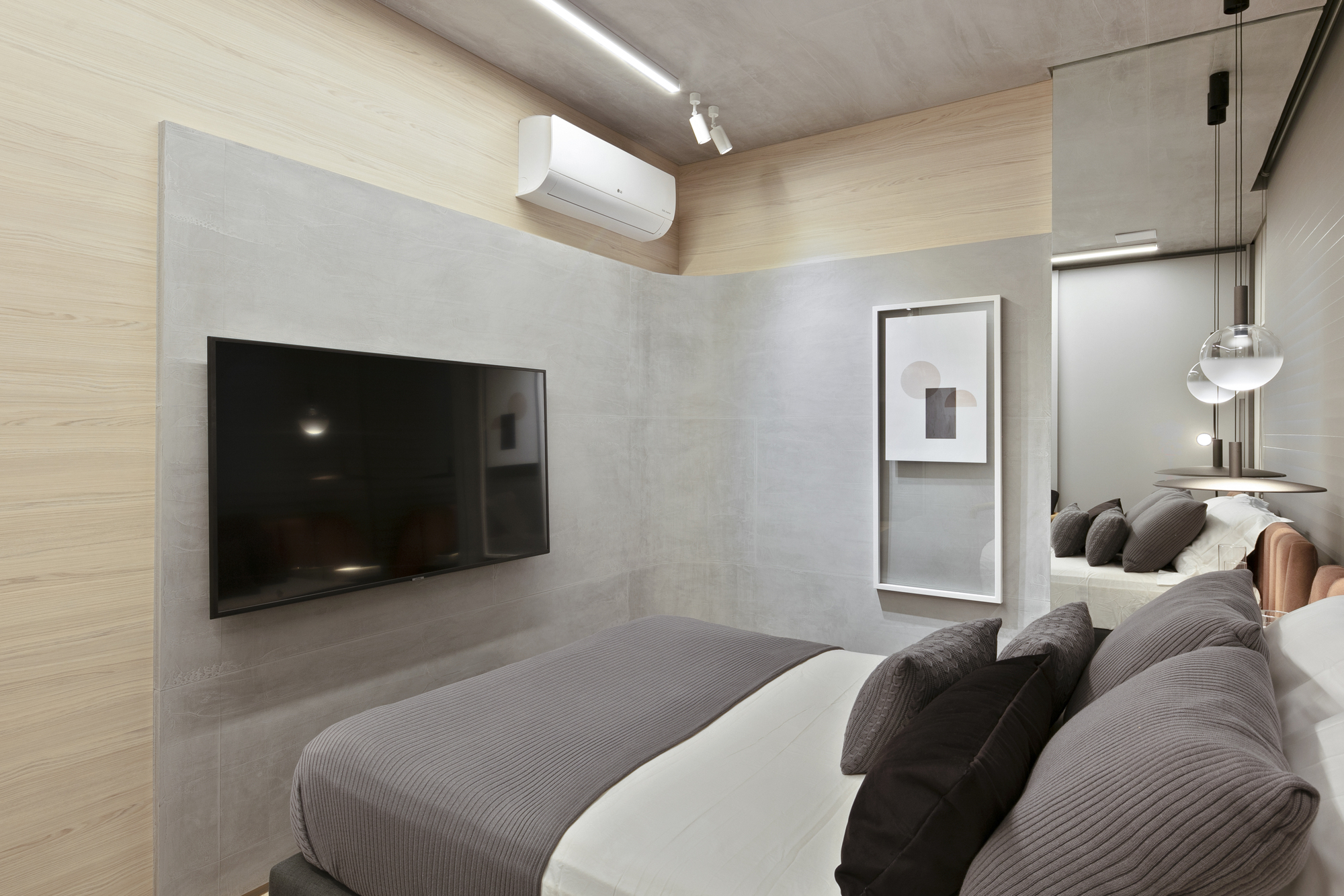 Bedroom corner with a wall-mounted television on a concrete-look panel, a wood-veneer wall and track lights along the ceiling