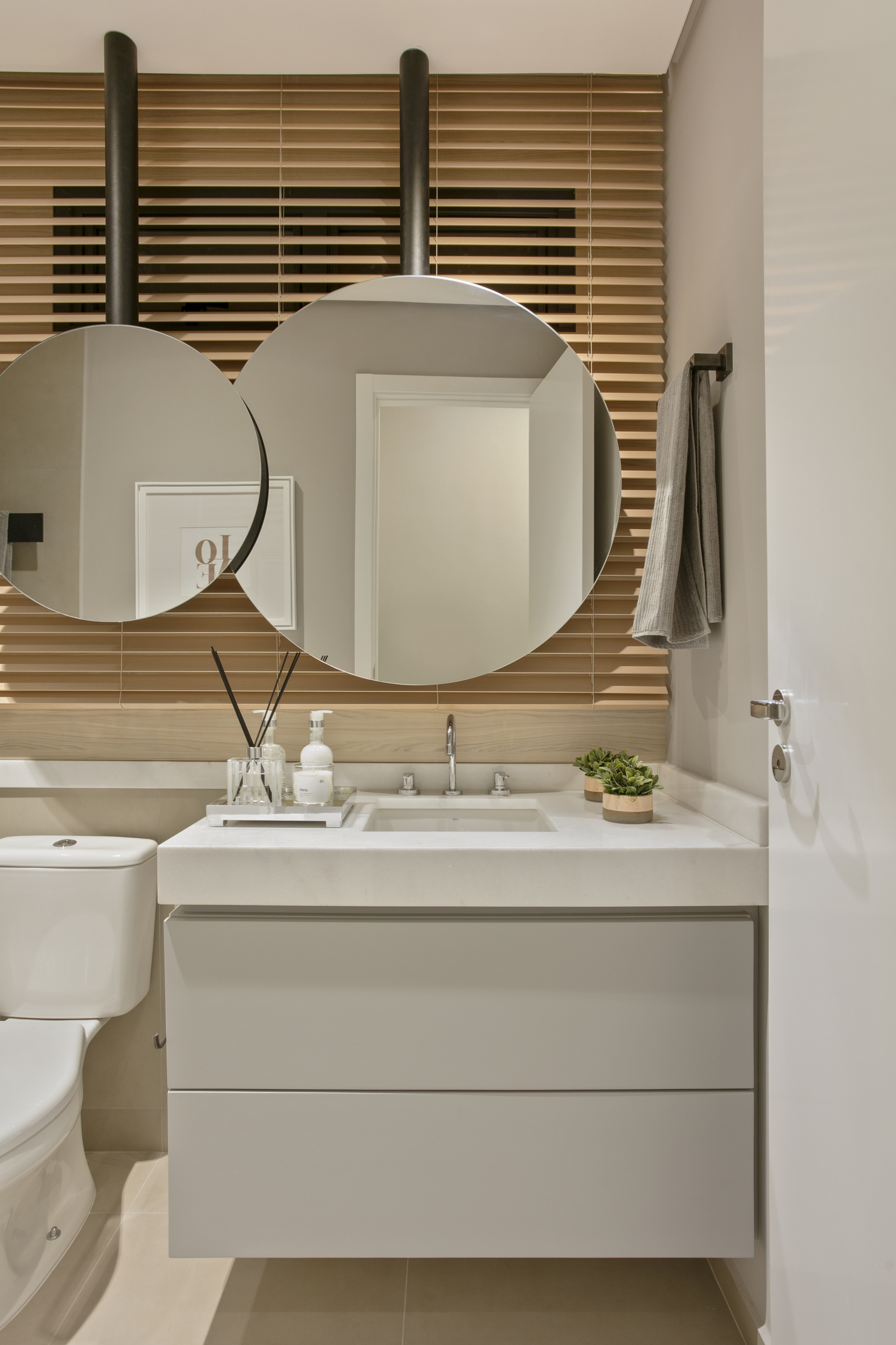 Powder room with two round mirrors hung from black rods in front of wooden slat blinds above a floating vanity