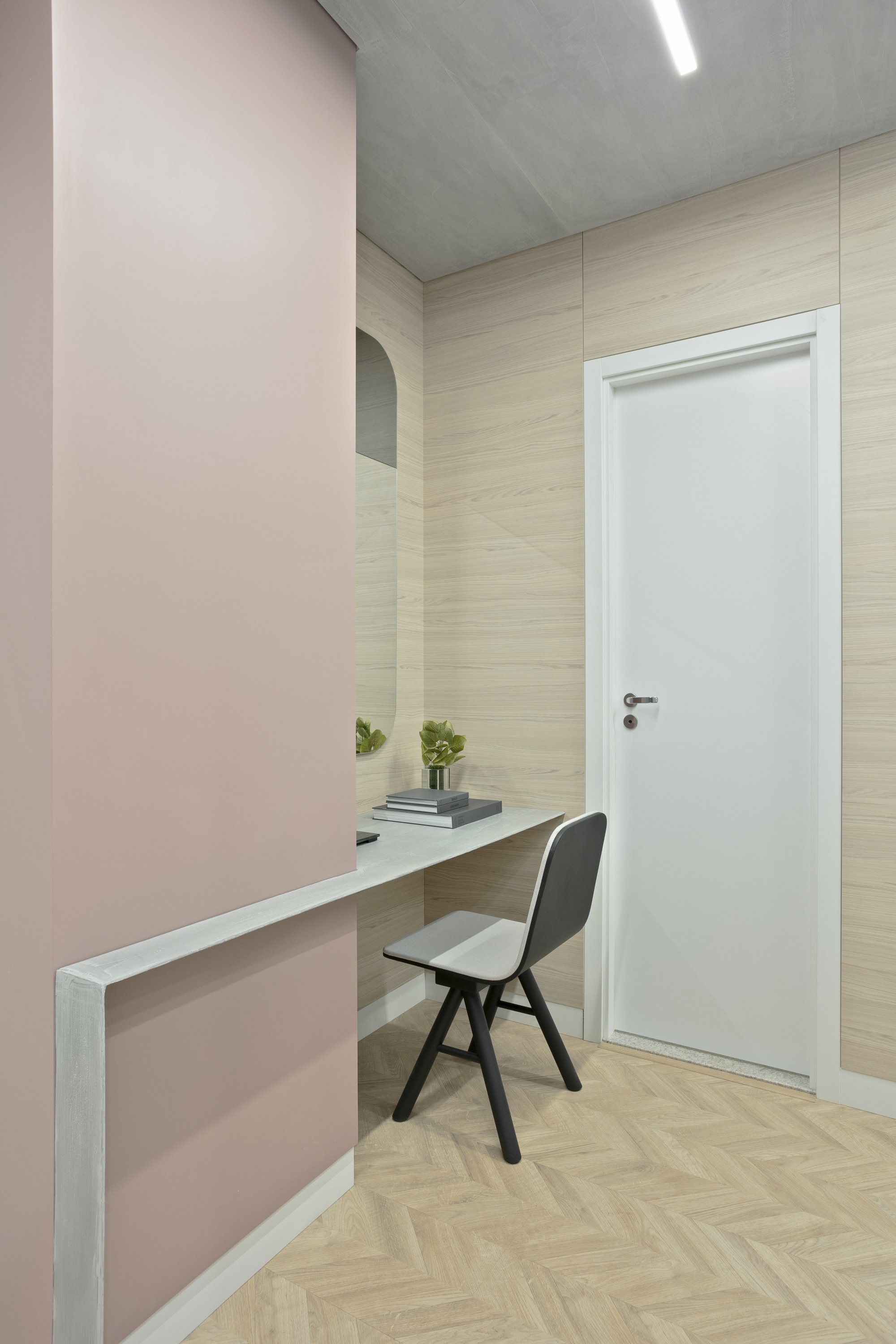 Built-in desk projecting from a dusty pink wall, with a grey chair and potted plants beside a white door
