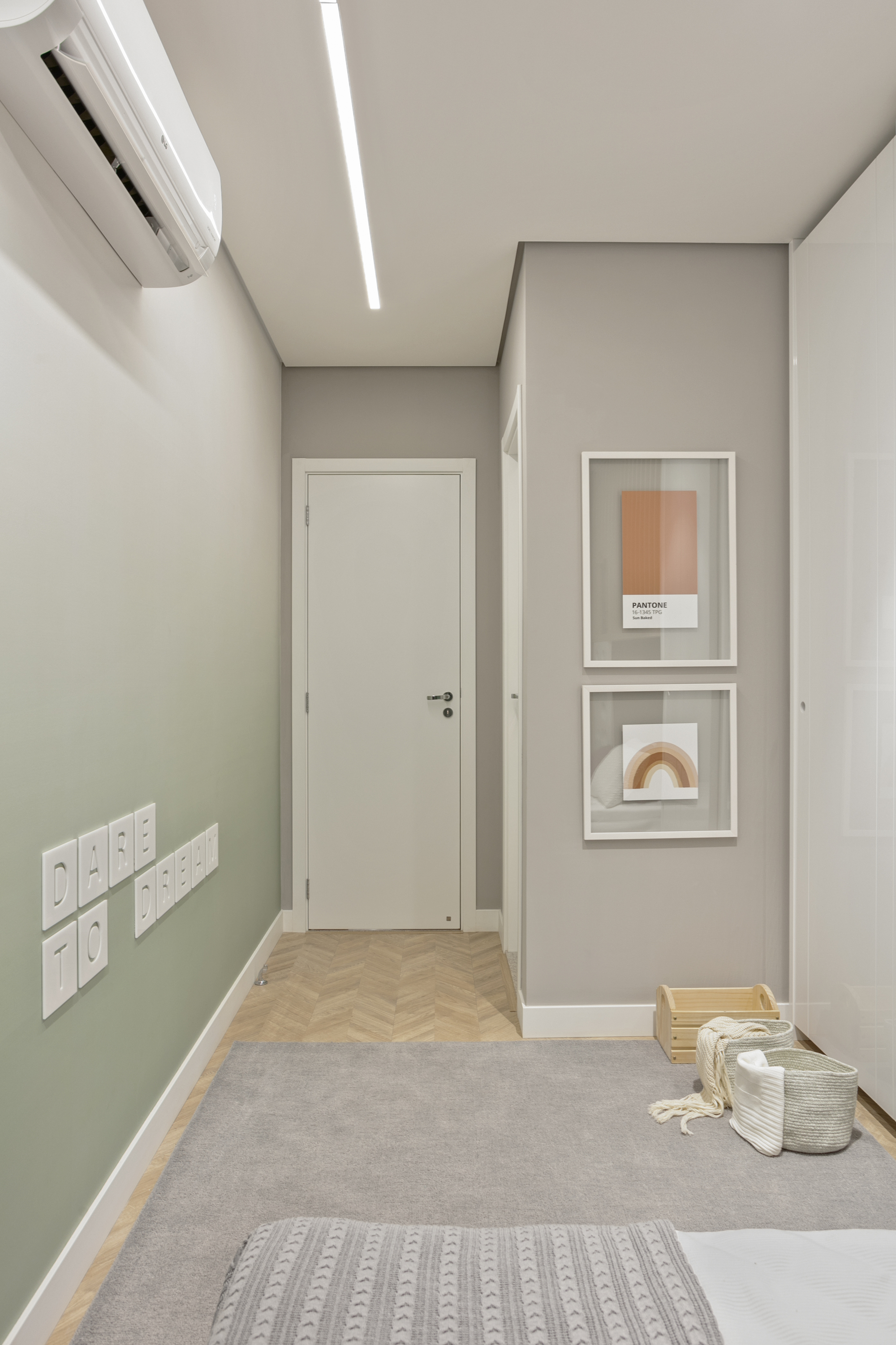 Narrow child's bedroom with a green gradient wall, letter-shaped switch plates, framed prints and a basket of toys on a grey rug