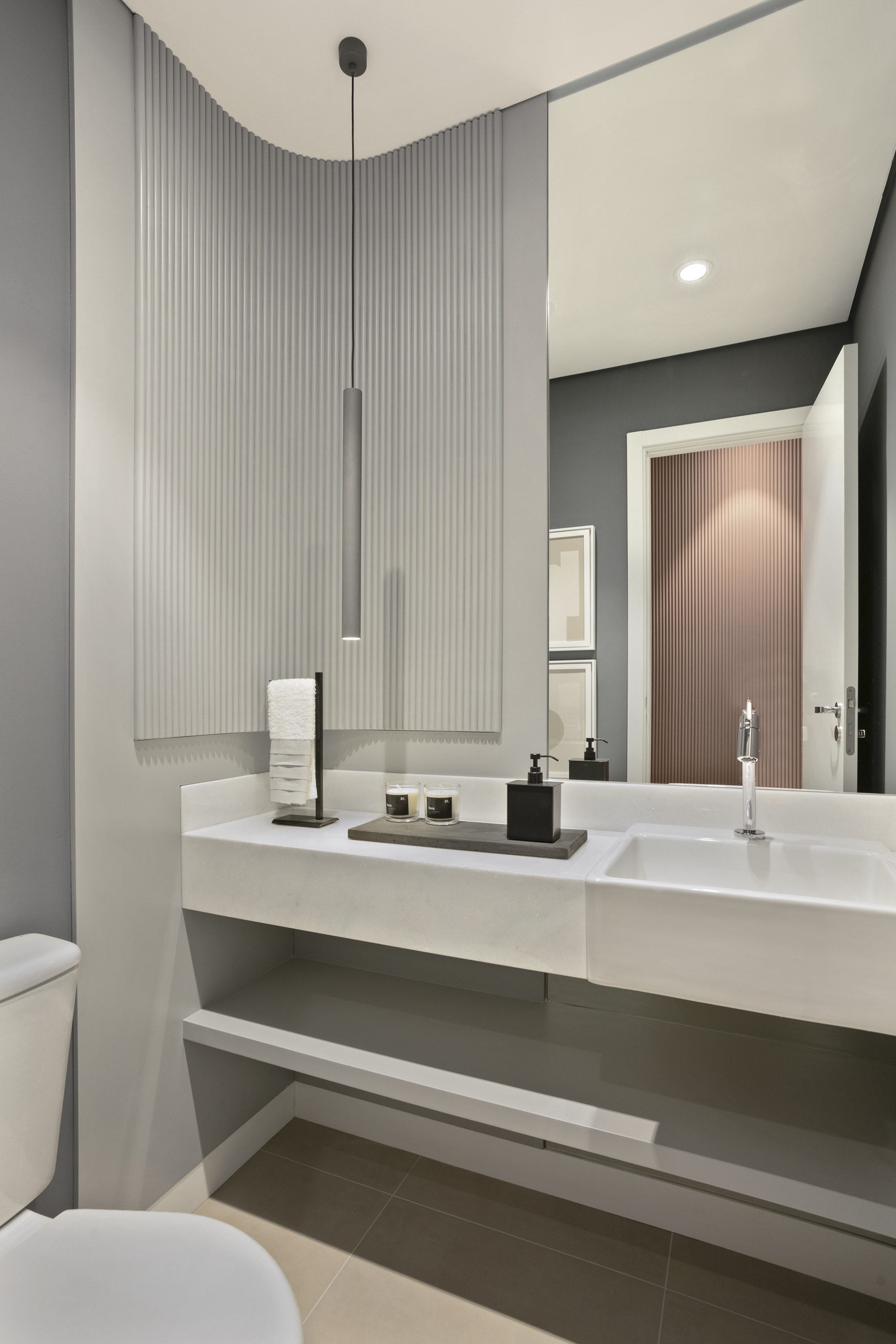 Powder room with a curved fluted wall panel, floating stone vanity, slim pendant light and a large mirror reflecting a pink fluted door