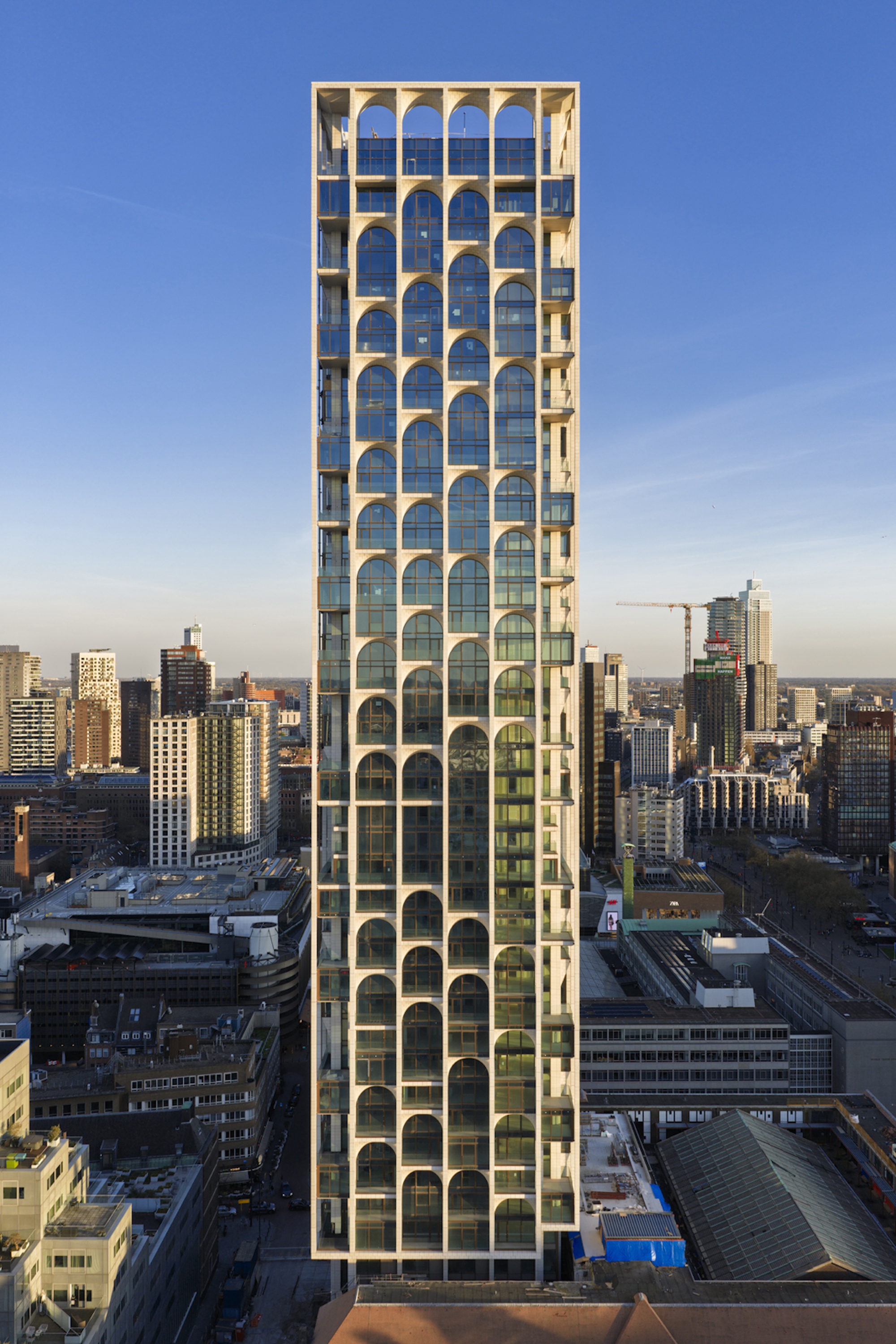 Frontal view of the slender tower with arched glazing between white frame members, against a clear blue evening sky
