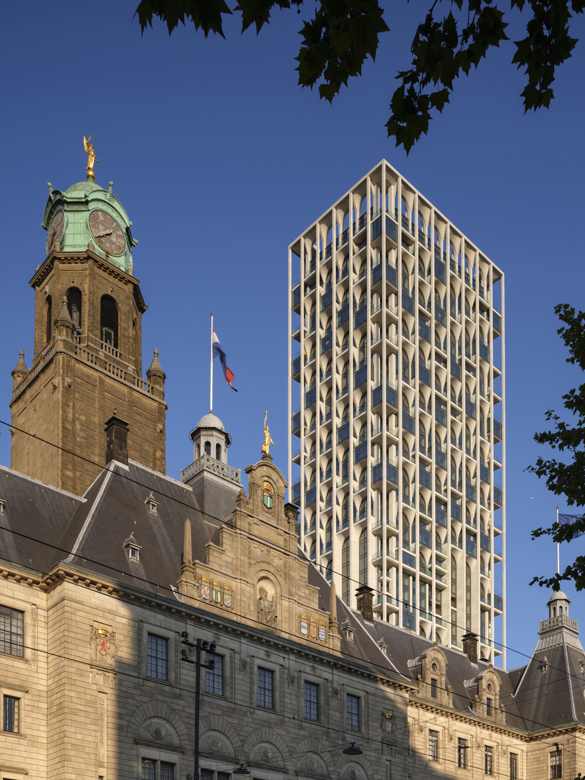 Tower with white lattice frame rising behind a historic stone town hall with green copper clock tower in low sun