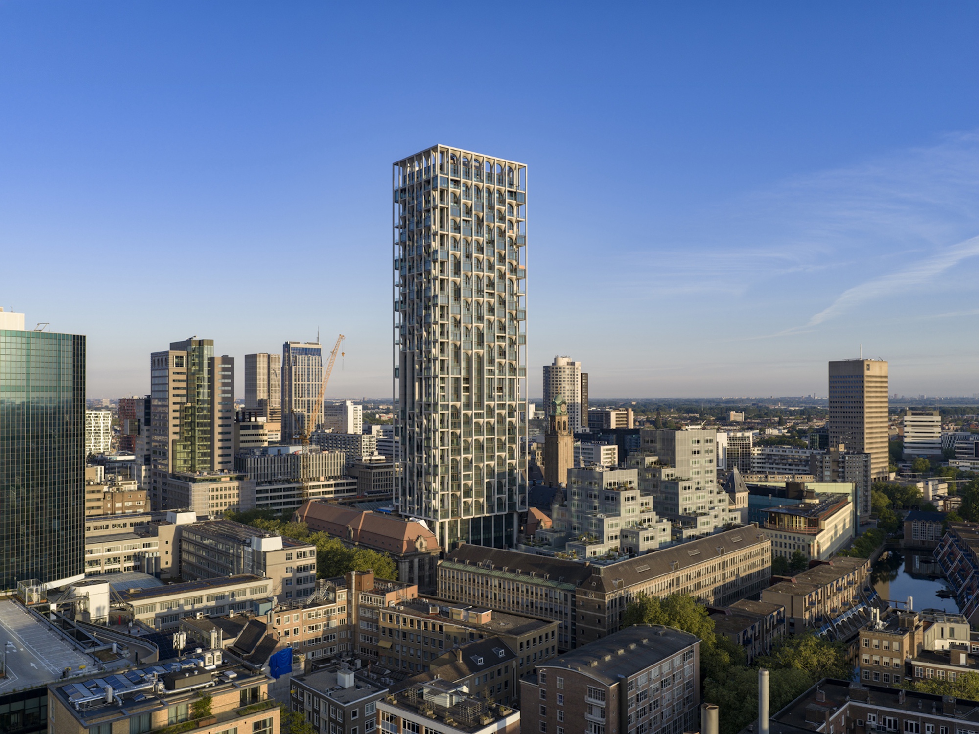 Tower rising above low brick rooftops and a canal, seen from above on a clear blue morning