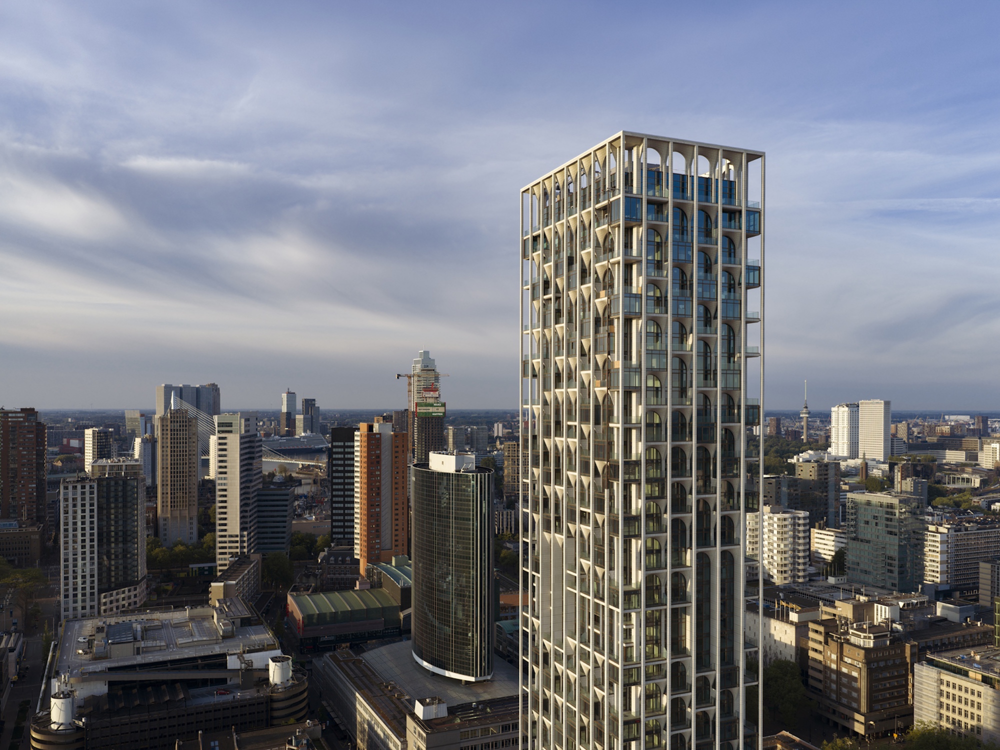 Upper floors of the white framed tower with arched openings beside a round glass tower, beneath streaked evening clouds