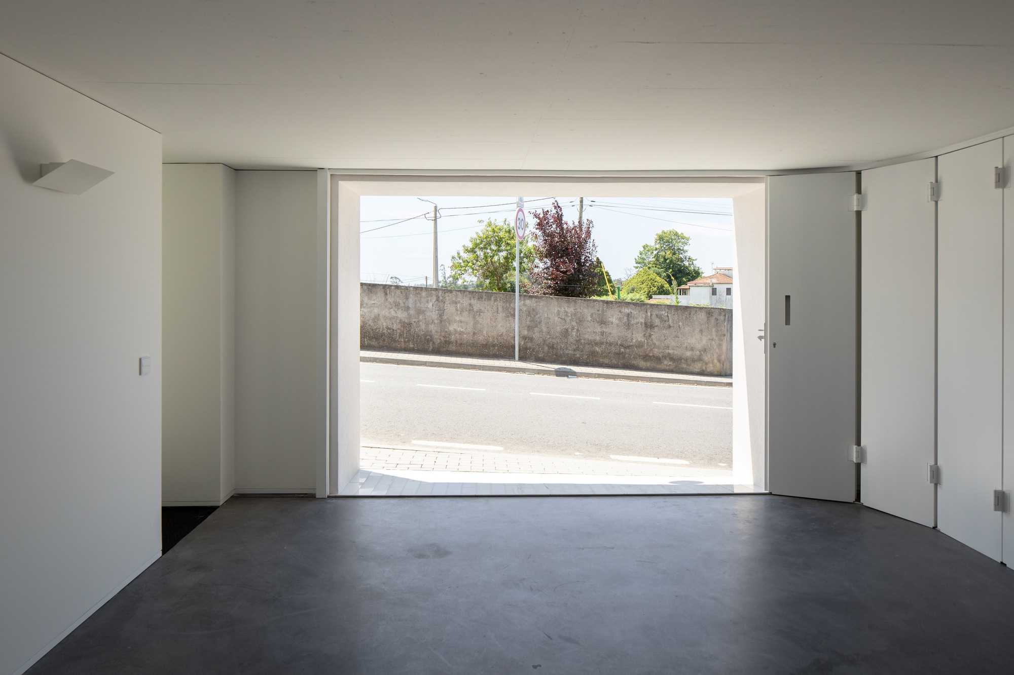 Interior with a polished concrete floor and a large opening with folding white panels, looking out to a road and a low wall