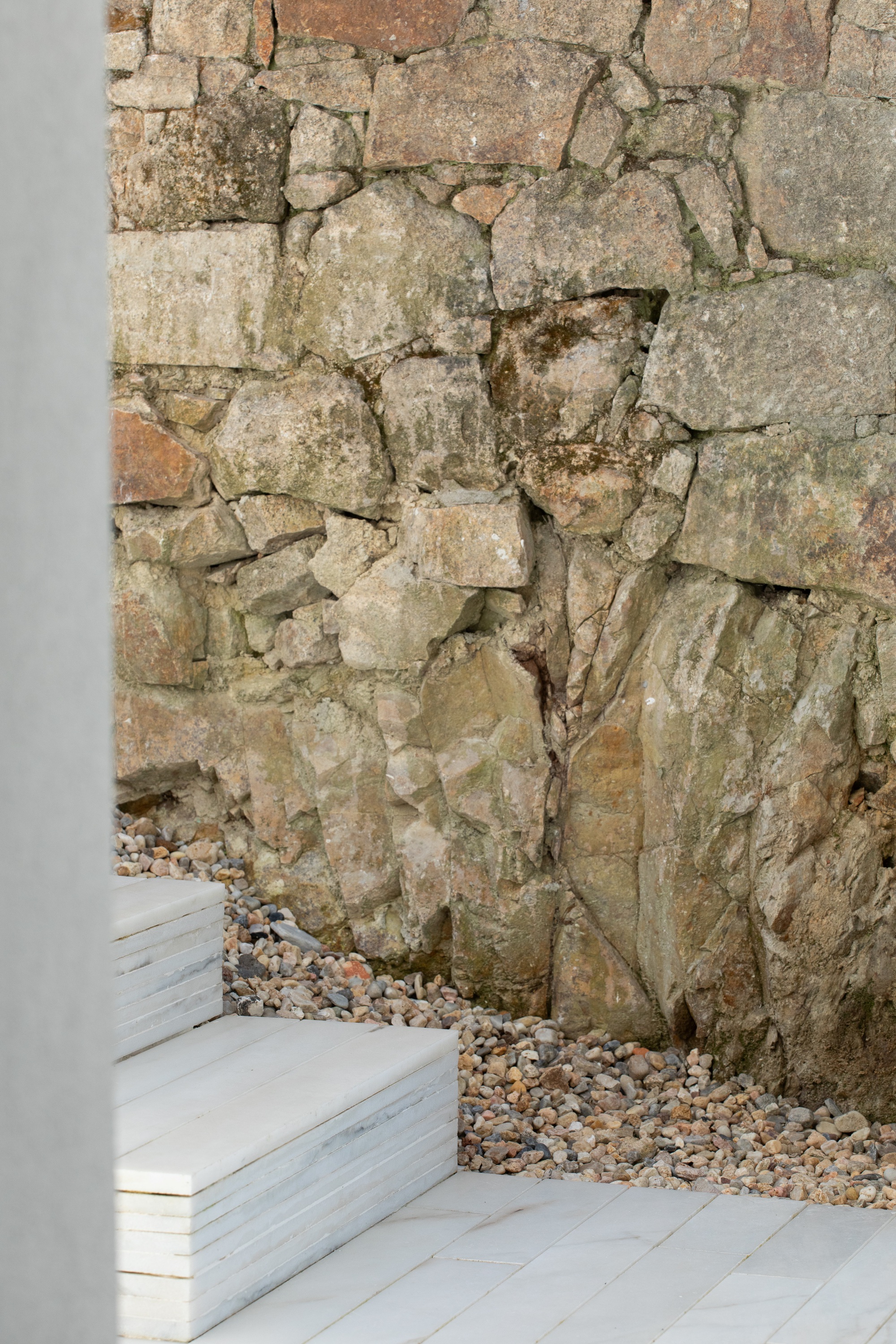 Rough granite retaining wall above pale marble steps and a gravel bed, with soft daylight raking across the stone
