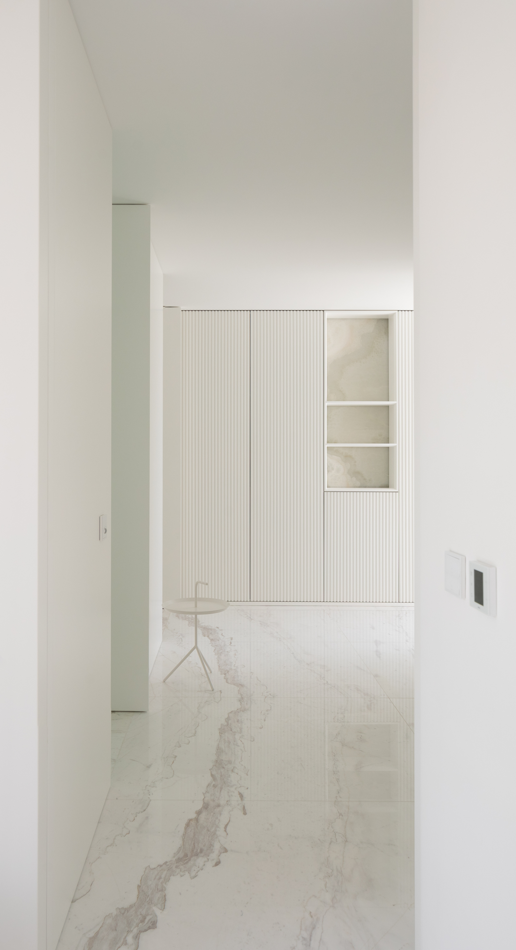 Hallway view toward fluted white cabinetry with an onyx-backed niche, and a thick-veined marble floor reflecting soft light
