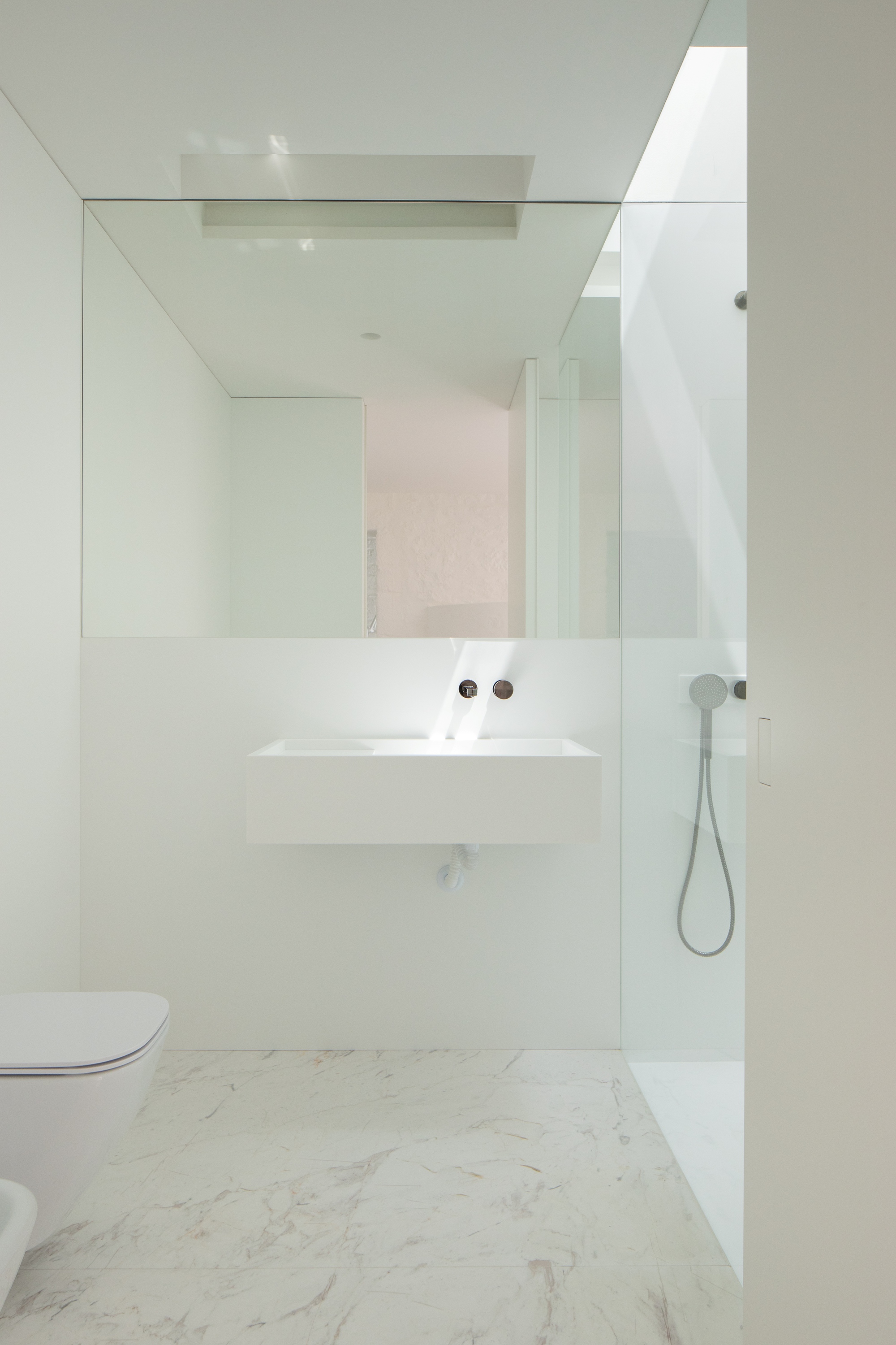 Bathroom with a wall-hung white basin, glass shower screen and marble floor, with daylight falling from a skylight
