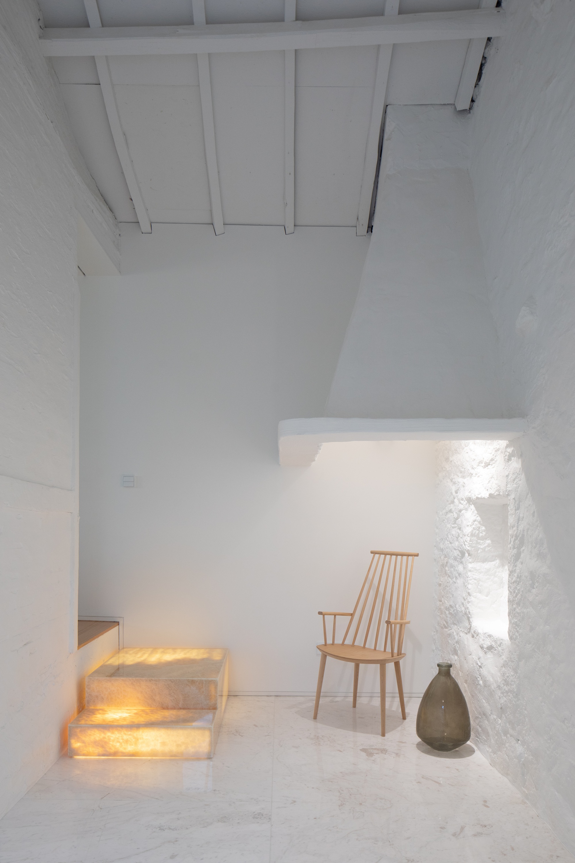 Whitewashed stone room with glowing onyx steps, a wooden chair and a glass vase on a marble floor