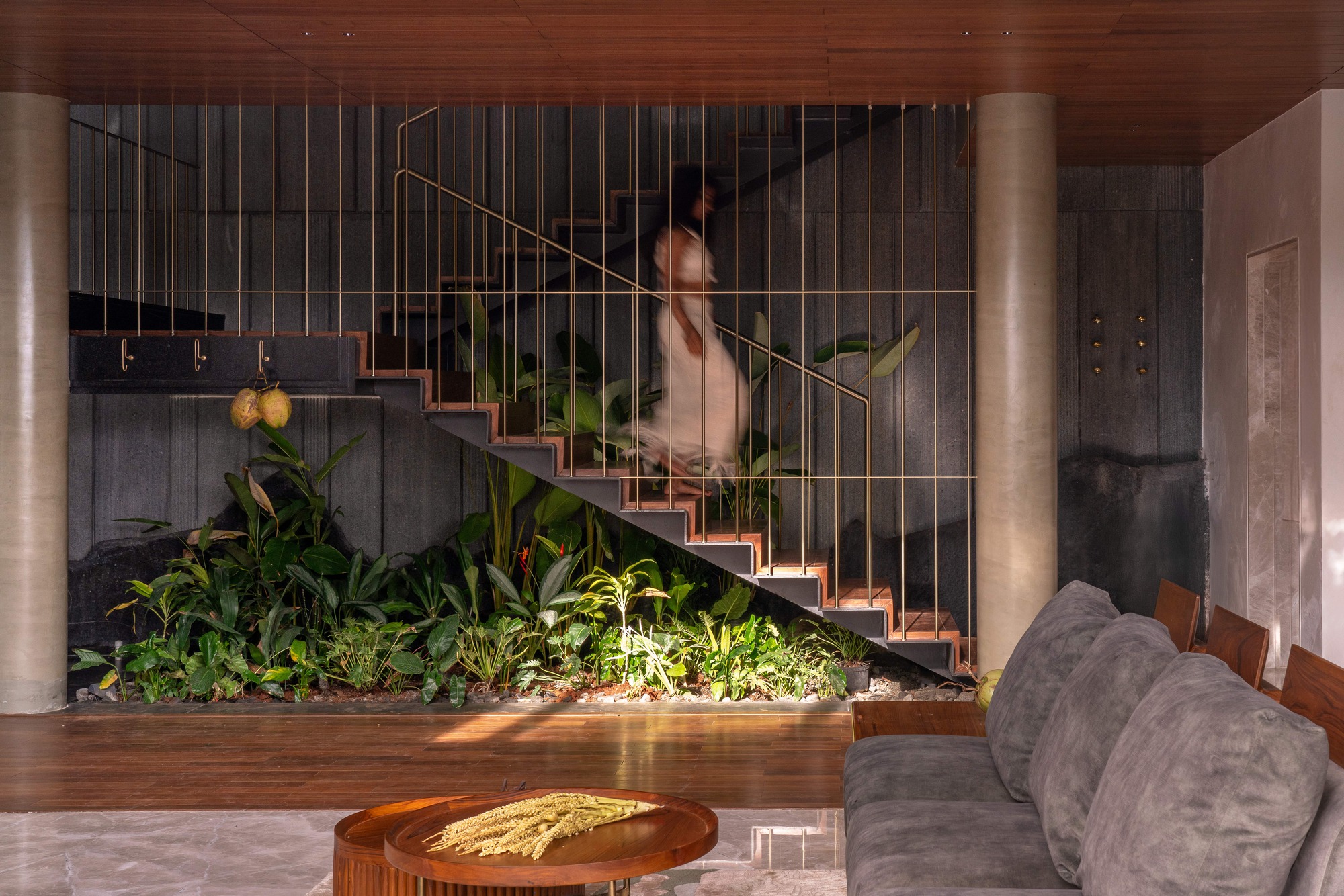 Steel staircase with slender brass balusters rising above a planted bed, a blurred figure descending in soft evening light