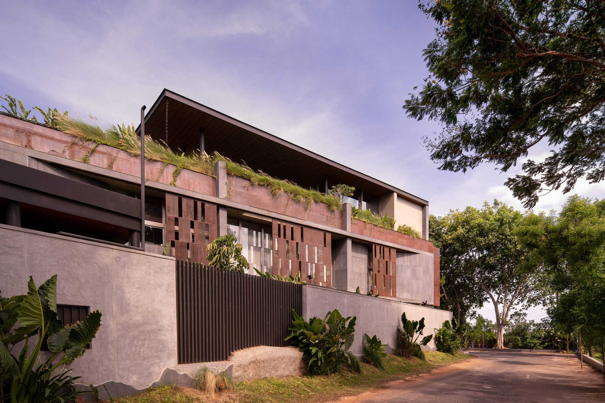 Side view of the stepped facade with rust-toned perforated screens and a grass-covered parapet, beside a road lined with trees