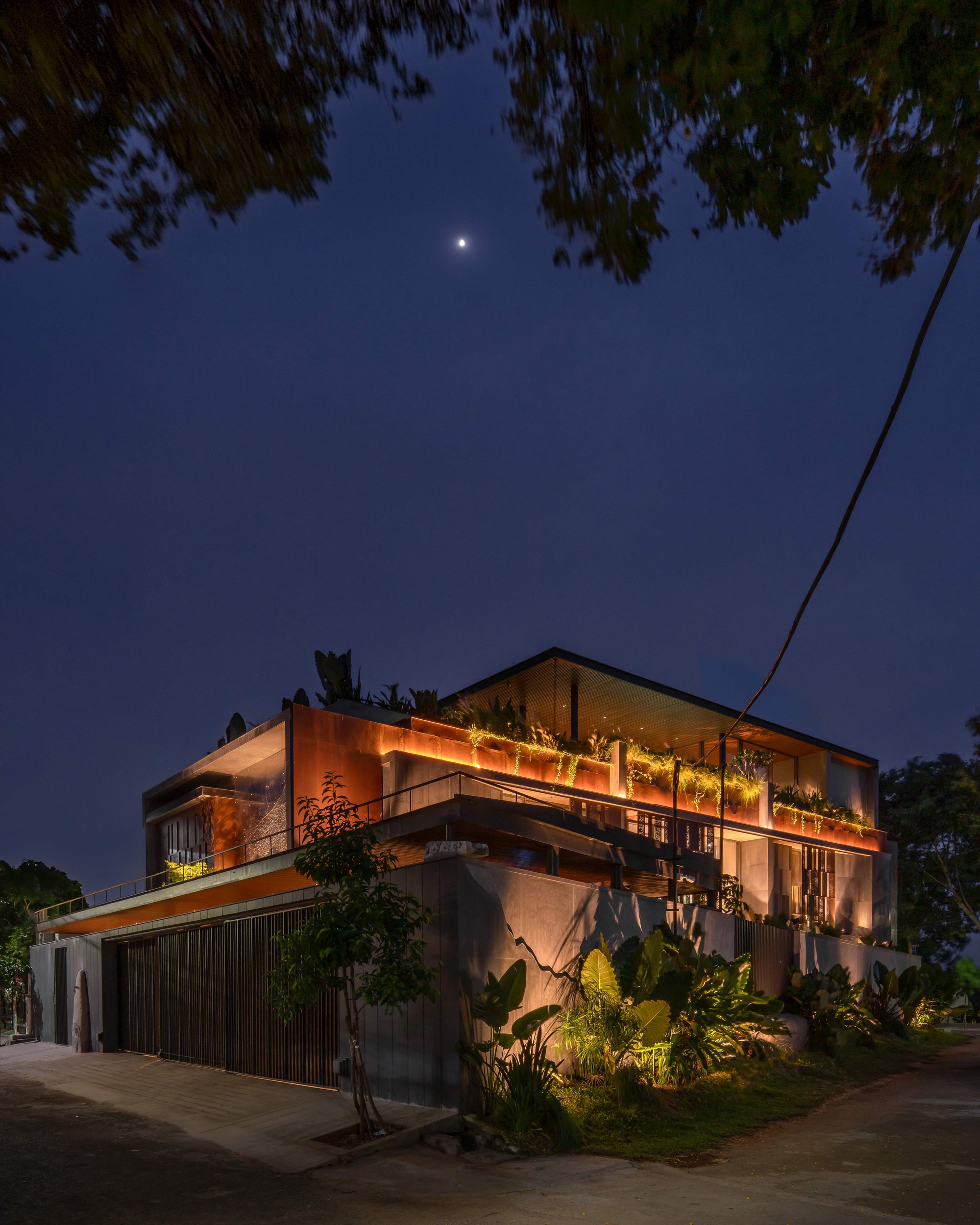 Corner of the house at night, with lit rooftop planters and a garage wall under a dark sky and a bright moon